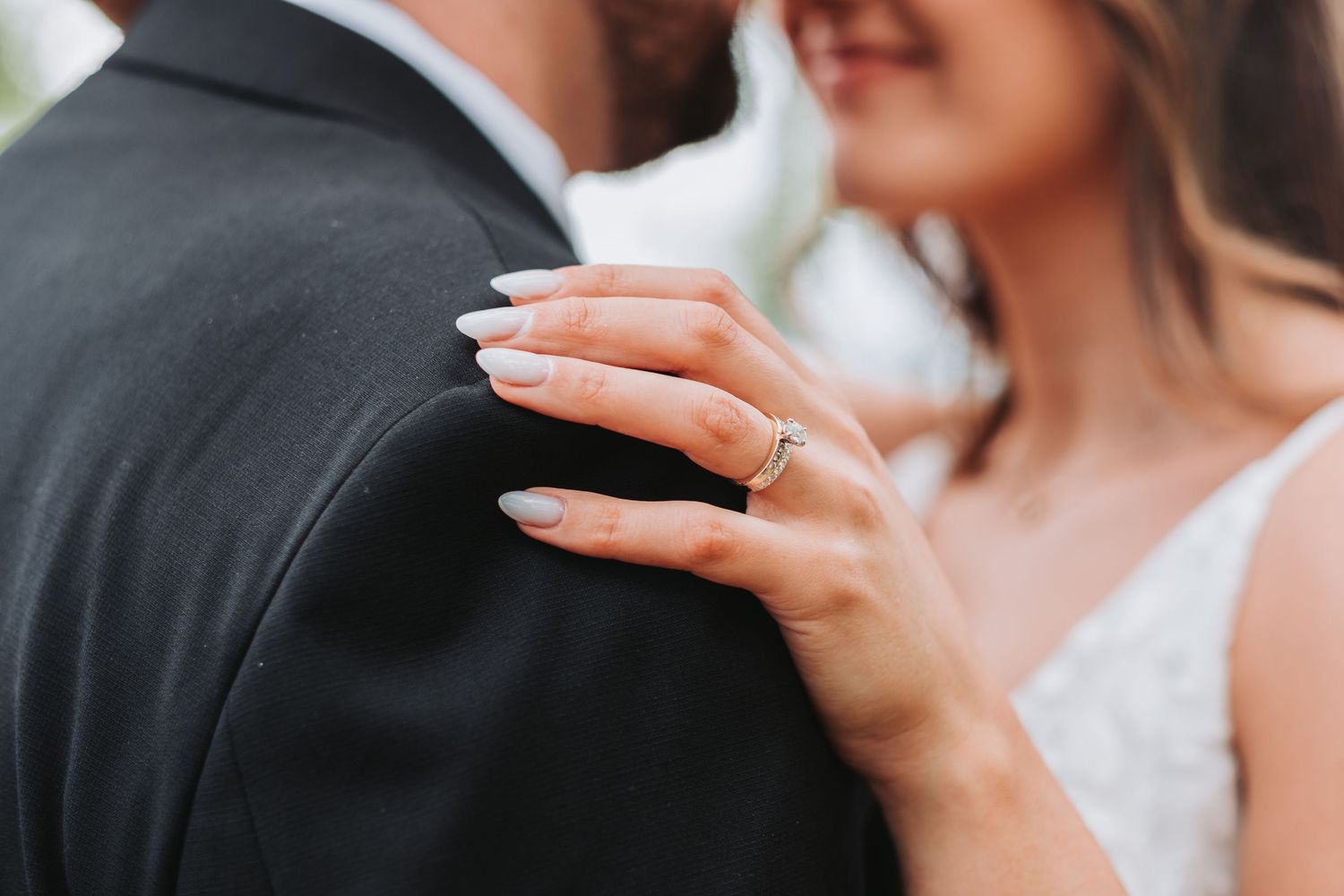 Close-up detail of a bride's hand with engagement ring resting on groom's dark suit during wedding ceremony.