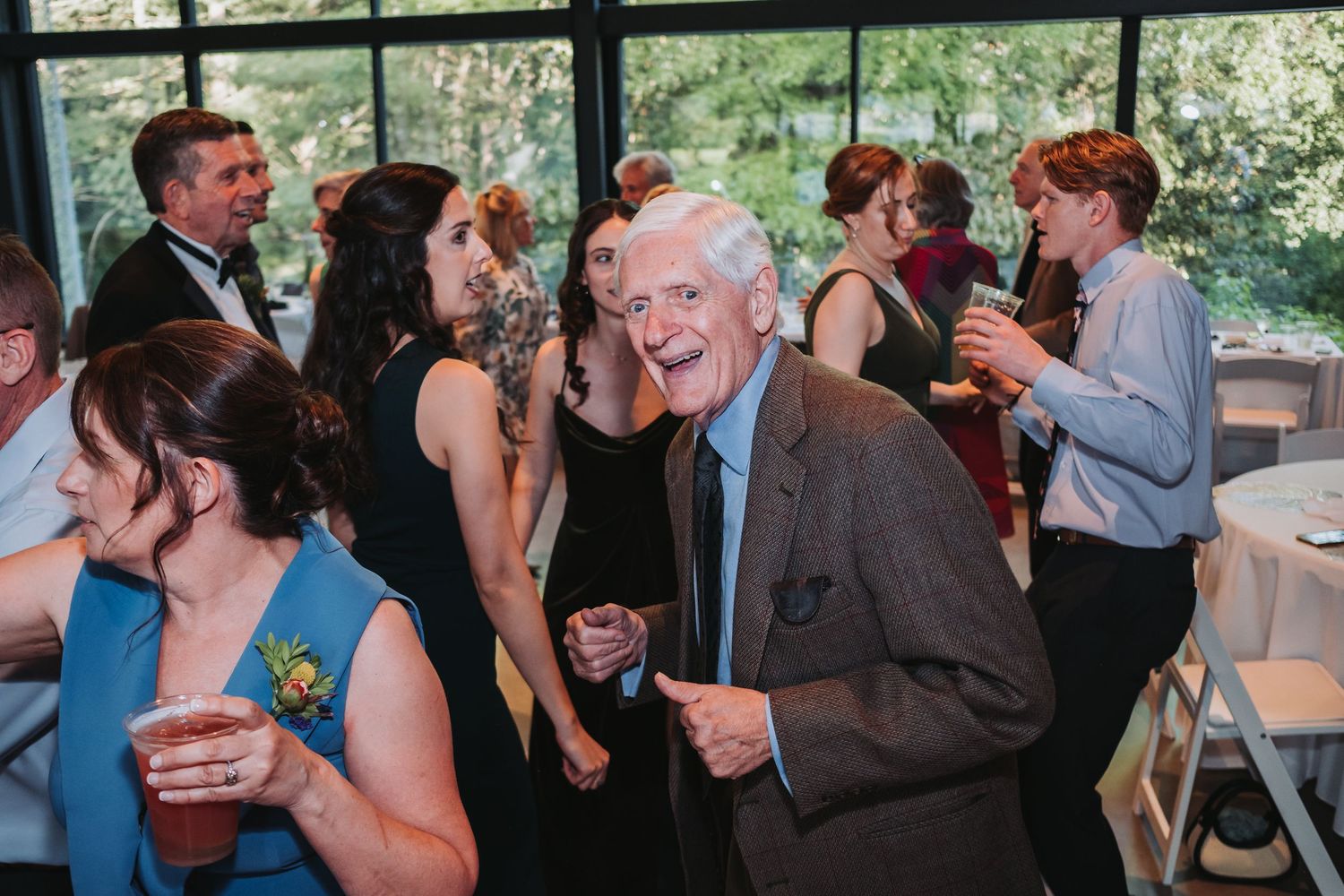 People dancing and socializing at what appears to be a wedding reception or celebration in a bright indoor venue.