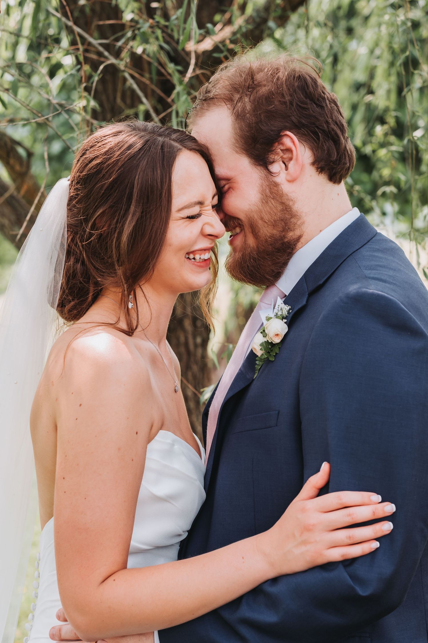 A couple shares an intimate moment on their wedding day outdoors with lush greenery in the background.