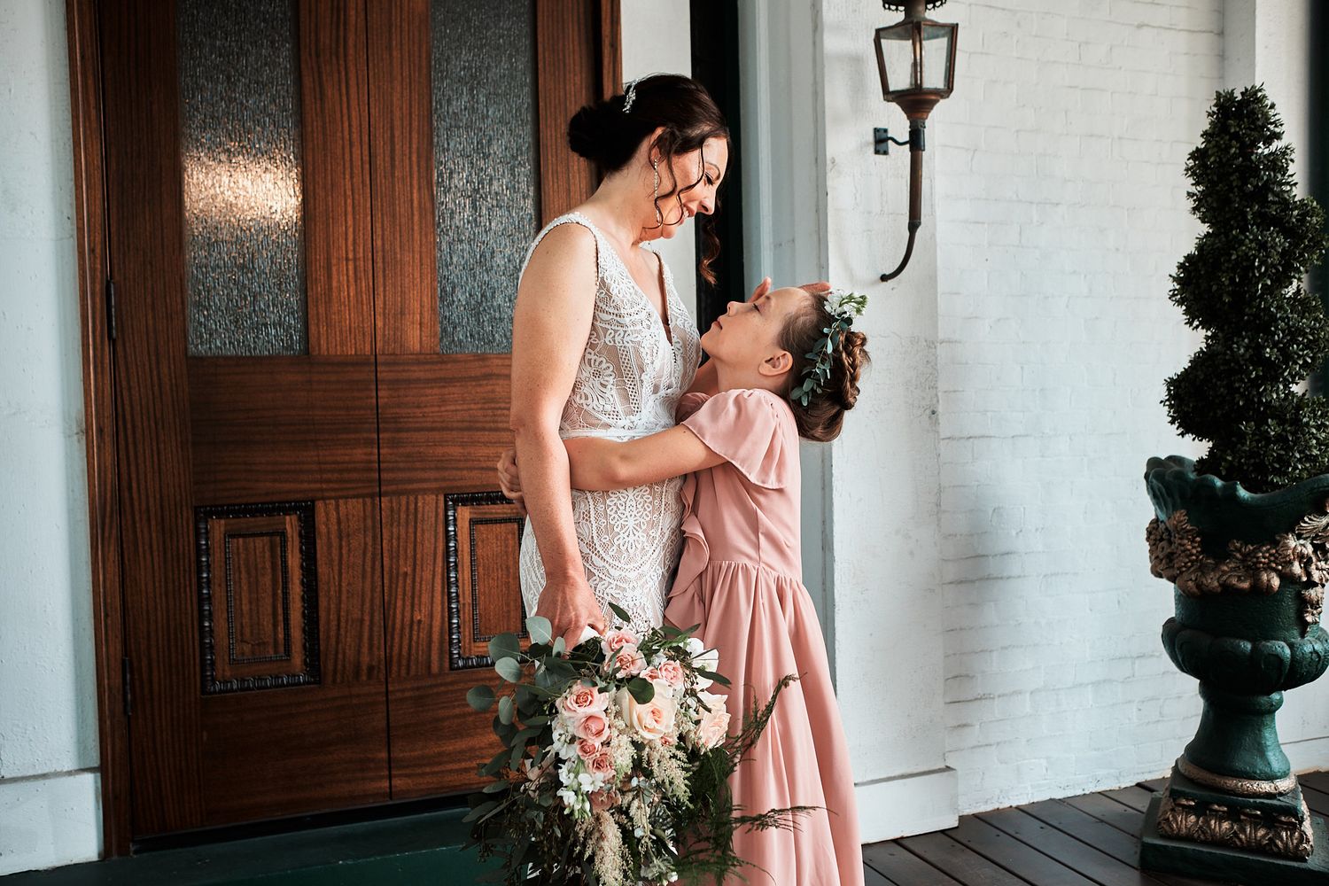 A tender moment on a porch with romantic blush florals, wooden door details, and vintage lighting.