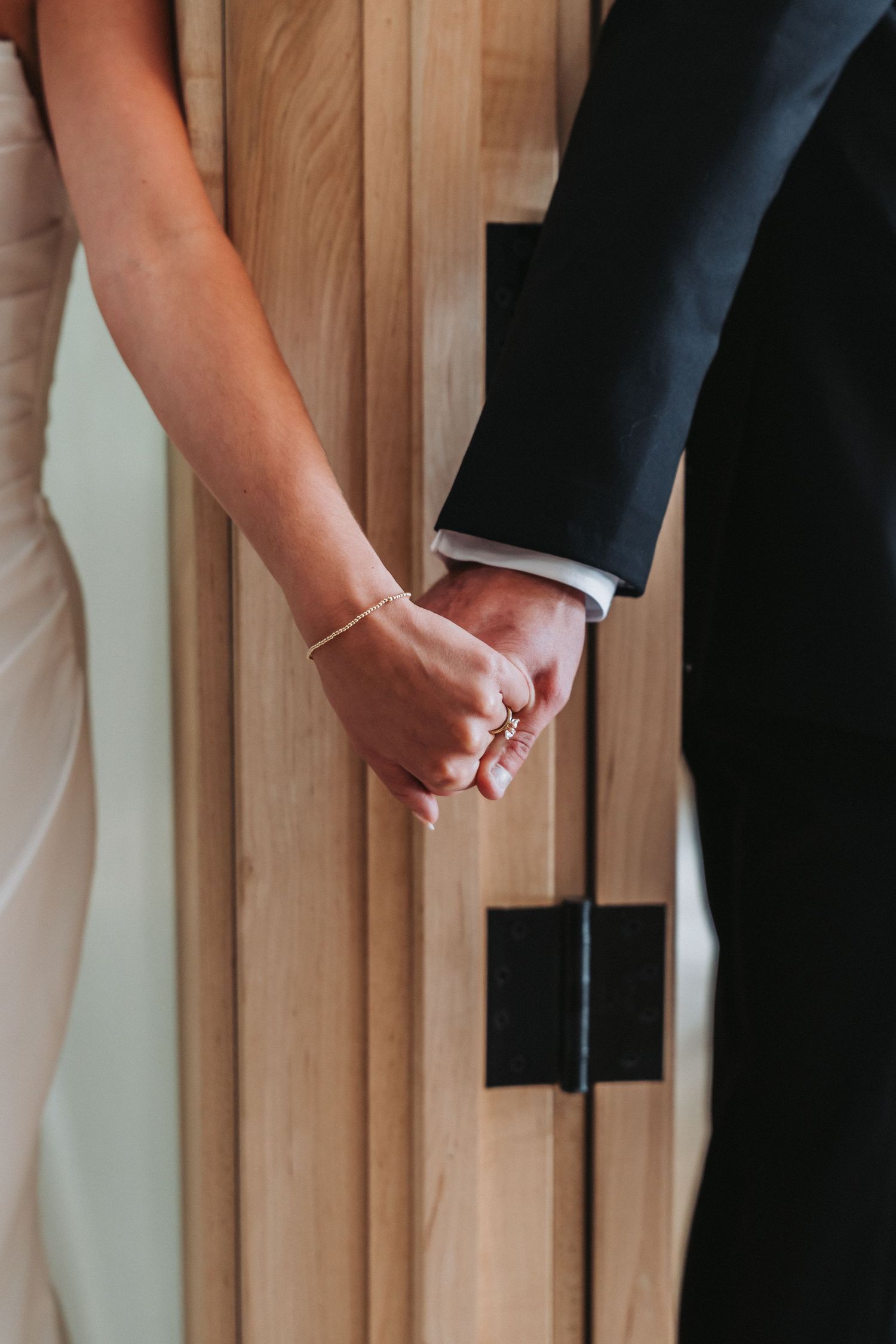 Close-up view of hands putting on a delicate silver bracelet against a wooden slat wall background.
