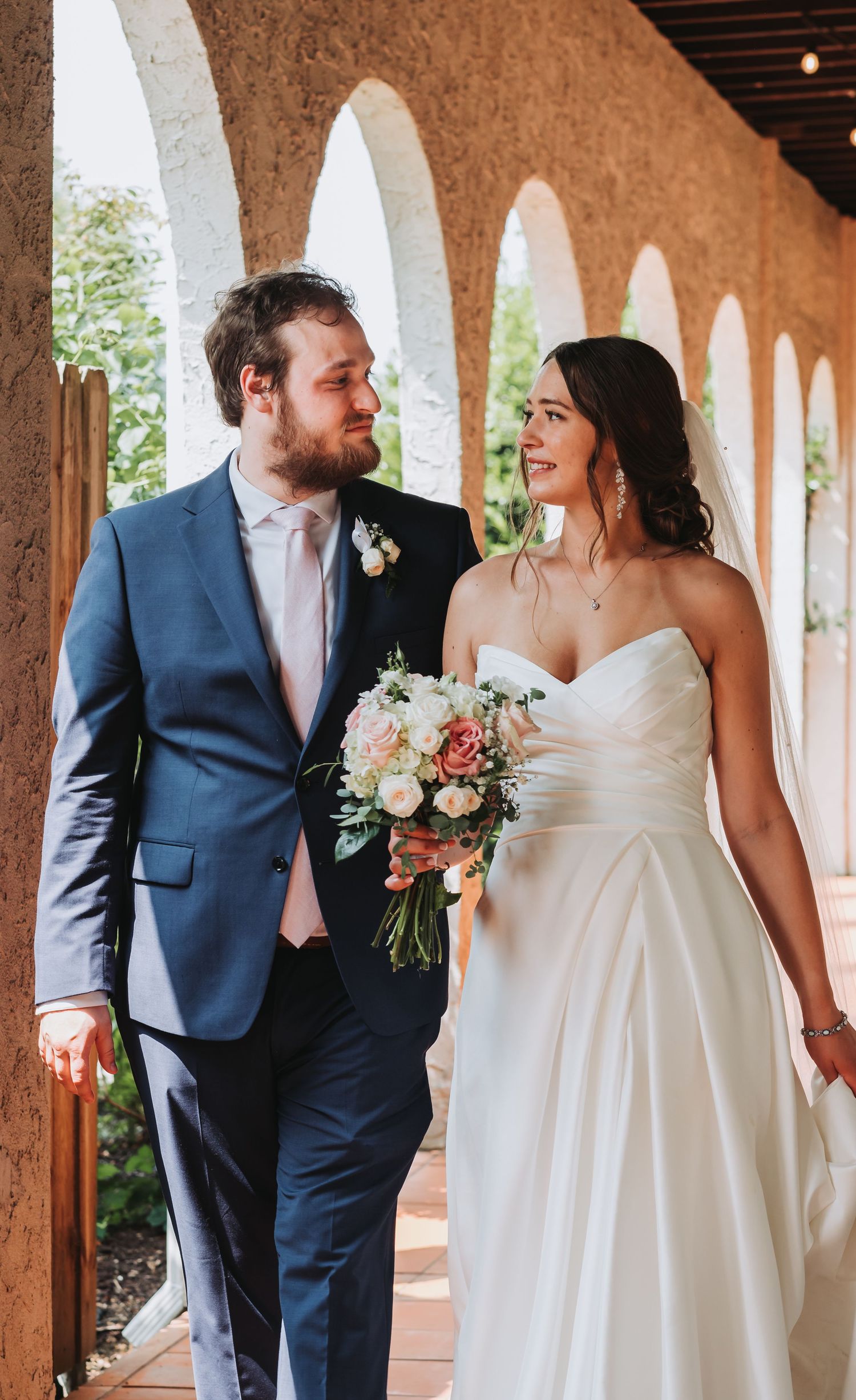 A couple in wedding attire sharing intimate moments under an outdoor colonnade with stone pillars and warm lighting.
