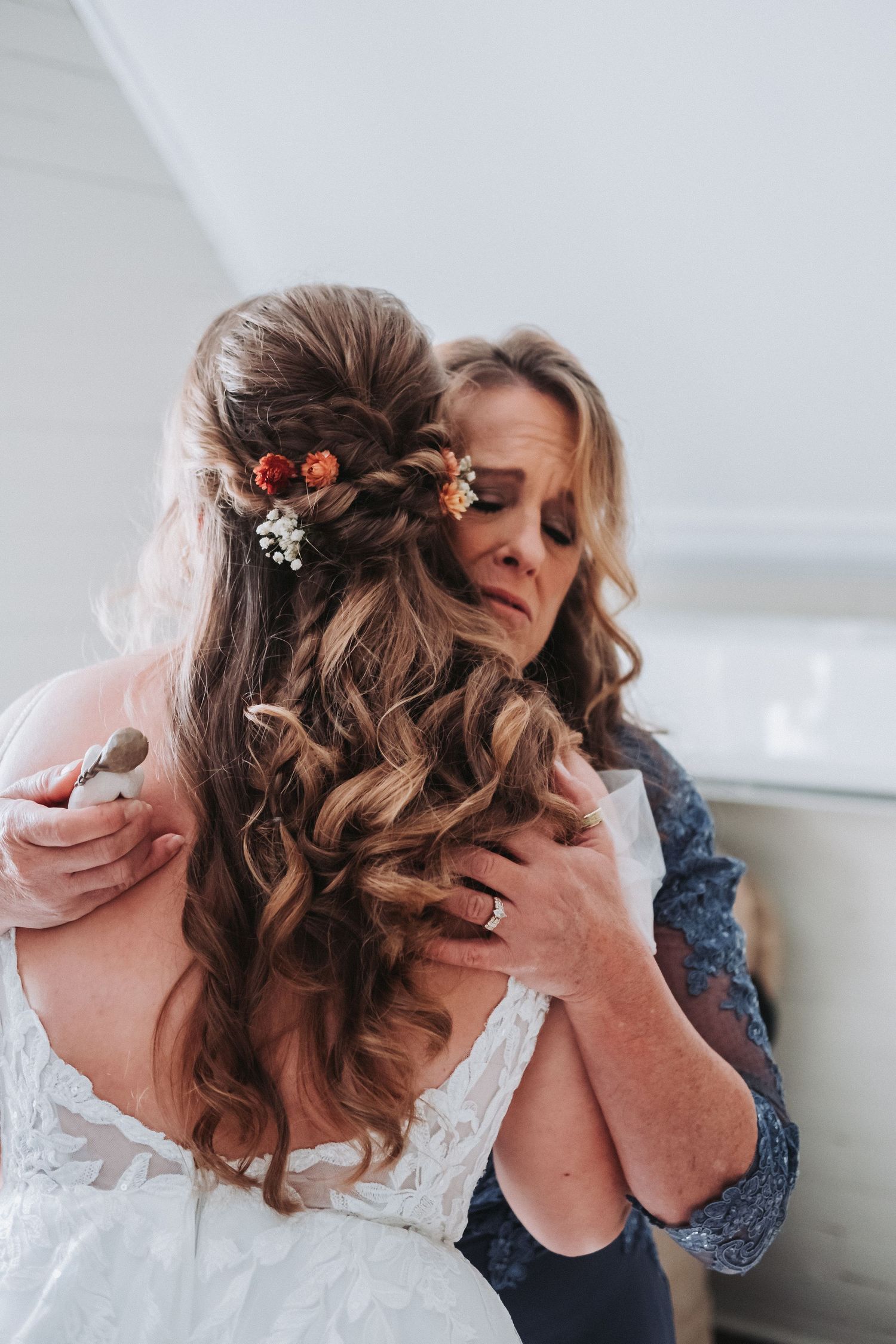 Emotional moment with elegant bridal hairstyle featuring long wavy curls adorned with floral accessories and sparkly details.