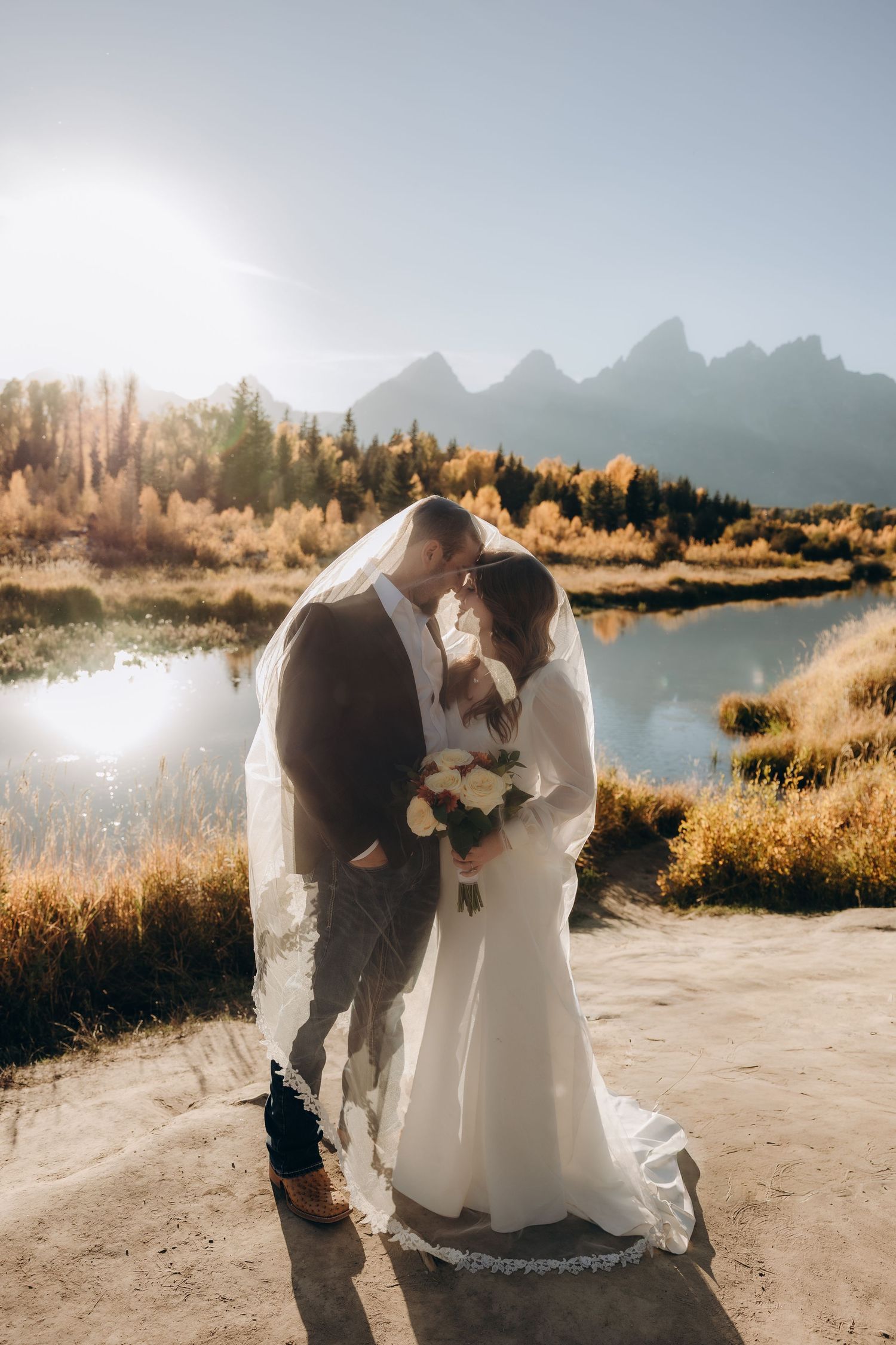 A couple shares an intimate moment during their wedding photoshoot with majestic mountains and autumn foliage in the background.