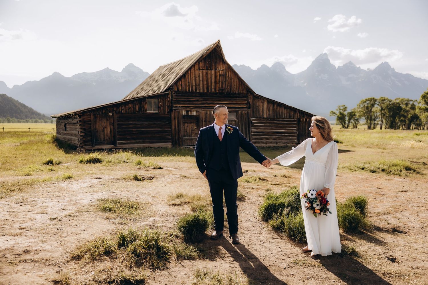 A rustic barn wedding photoshoot in a scenic mountain landscape with dramatic peaks in the background.