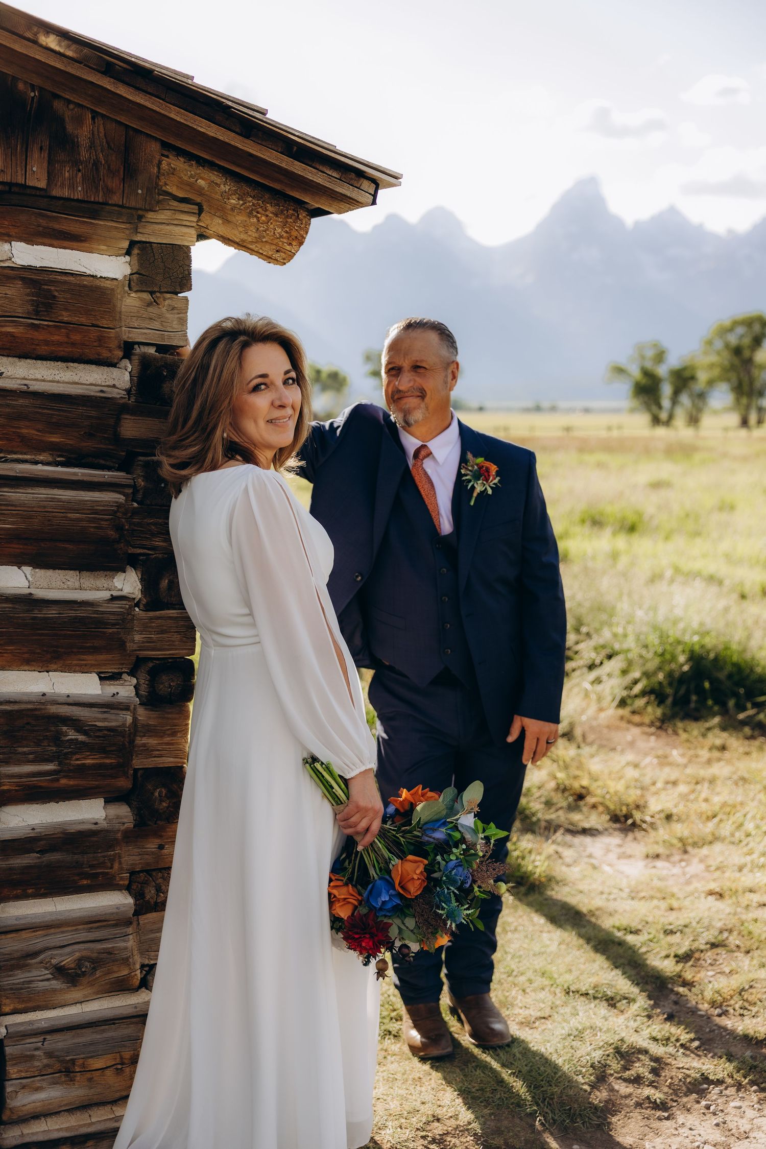 A couple shares intimate moments outside a rustic wooden cabin with majestic mountain peaks in the background.
