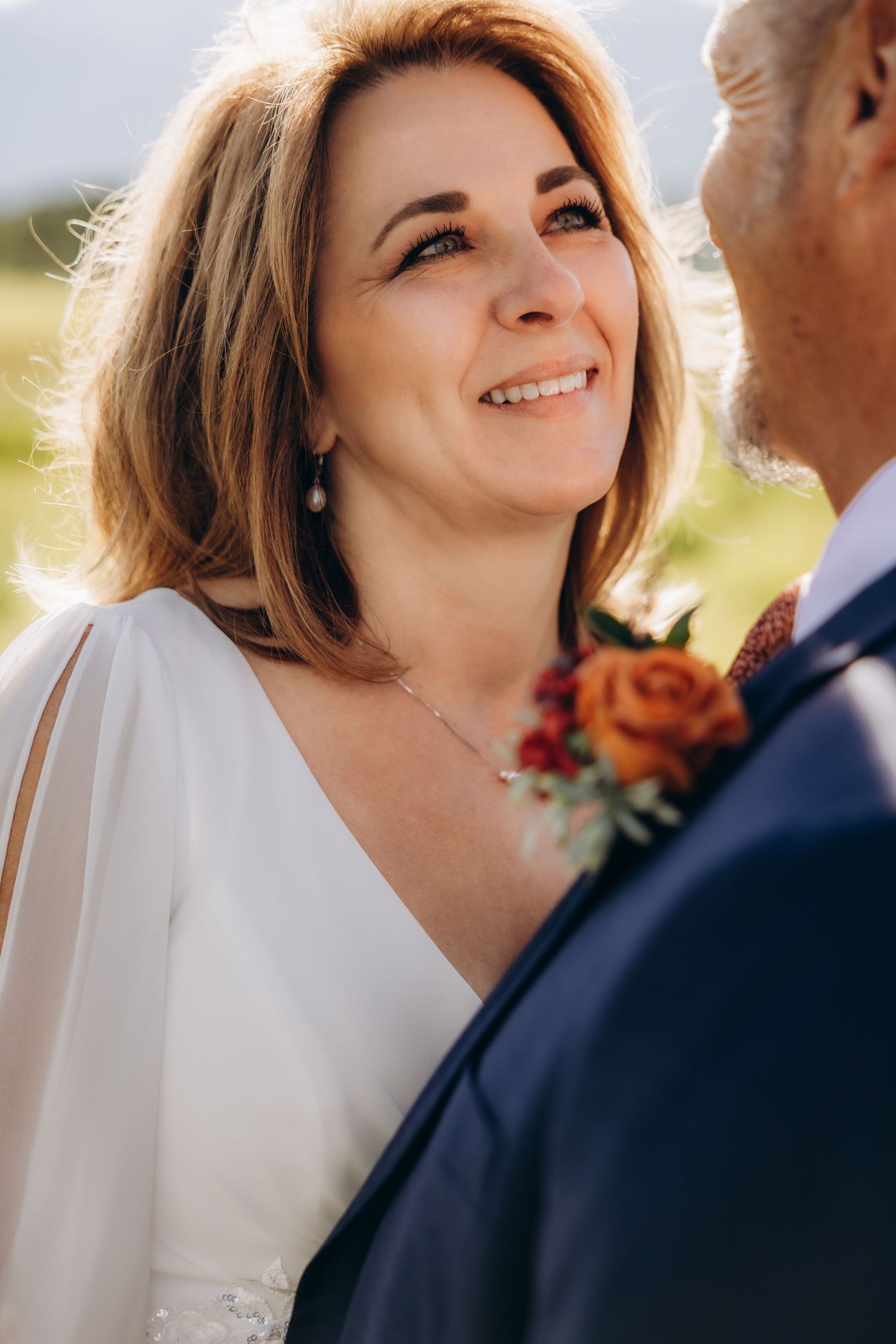 A bride in a white dress and short blonde hair shares joyful moments with her groom in a navy suit outdoors.