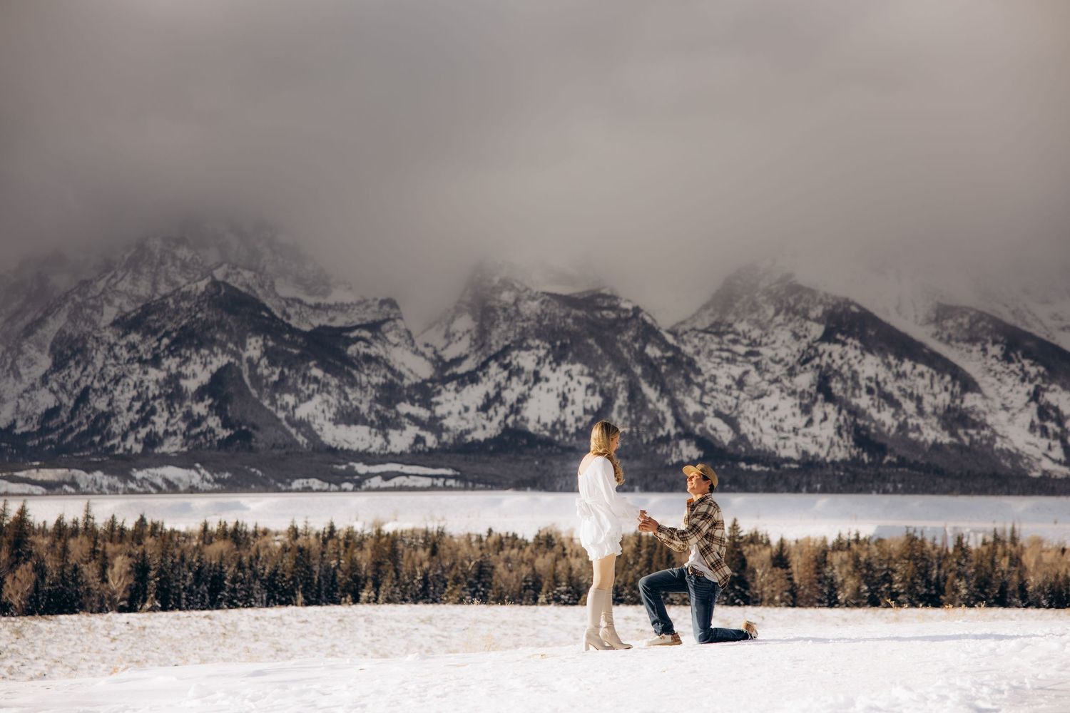 A winter proposal scene unfolds against snow-capped Teton mountains with golden light illuminating the snowy landscape.