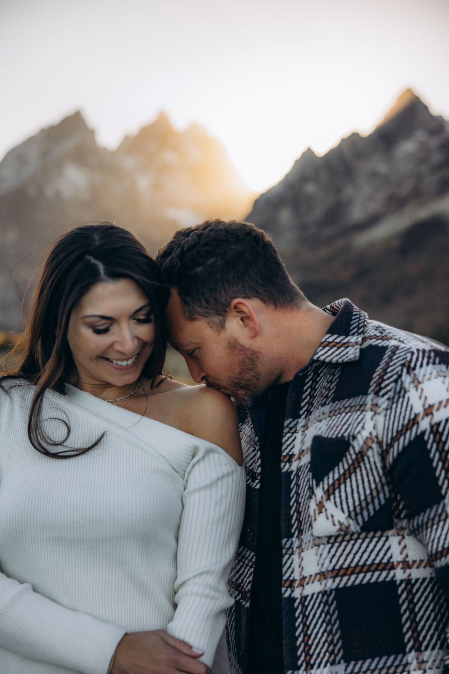 A romantic couple shares an intimate moment in front of mountain peaks during golden hour.