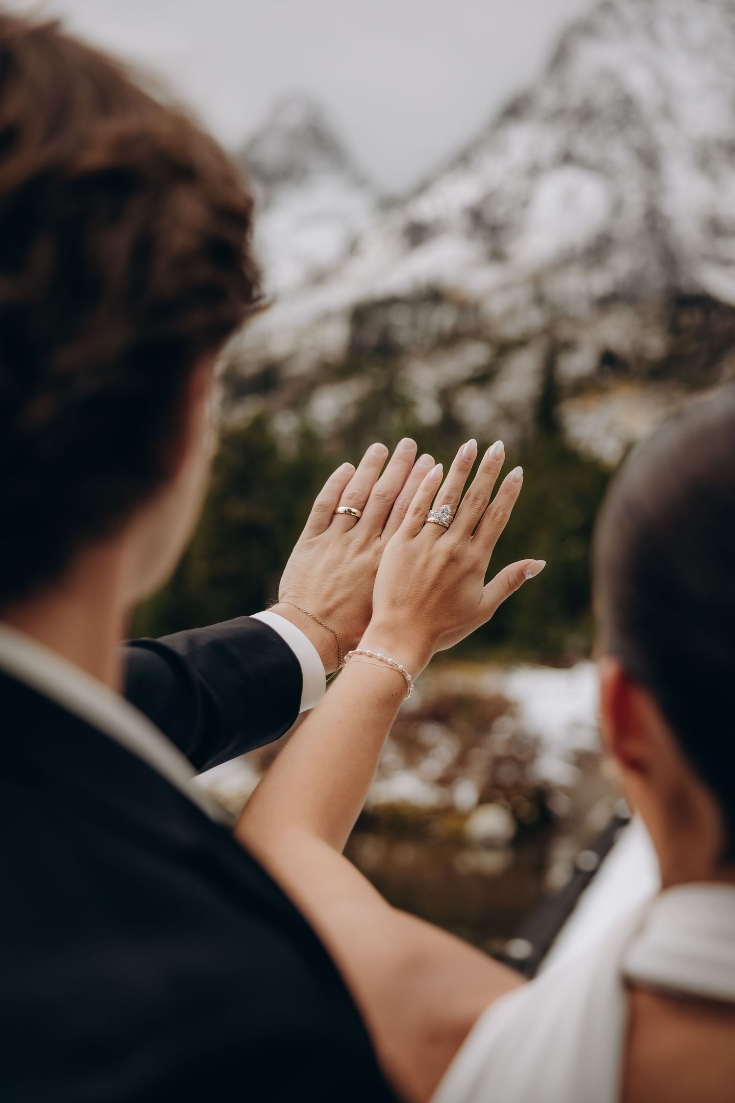 Two hands held up against a mountain backdrop showing matching wedding rings in natural lighting.
