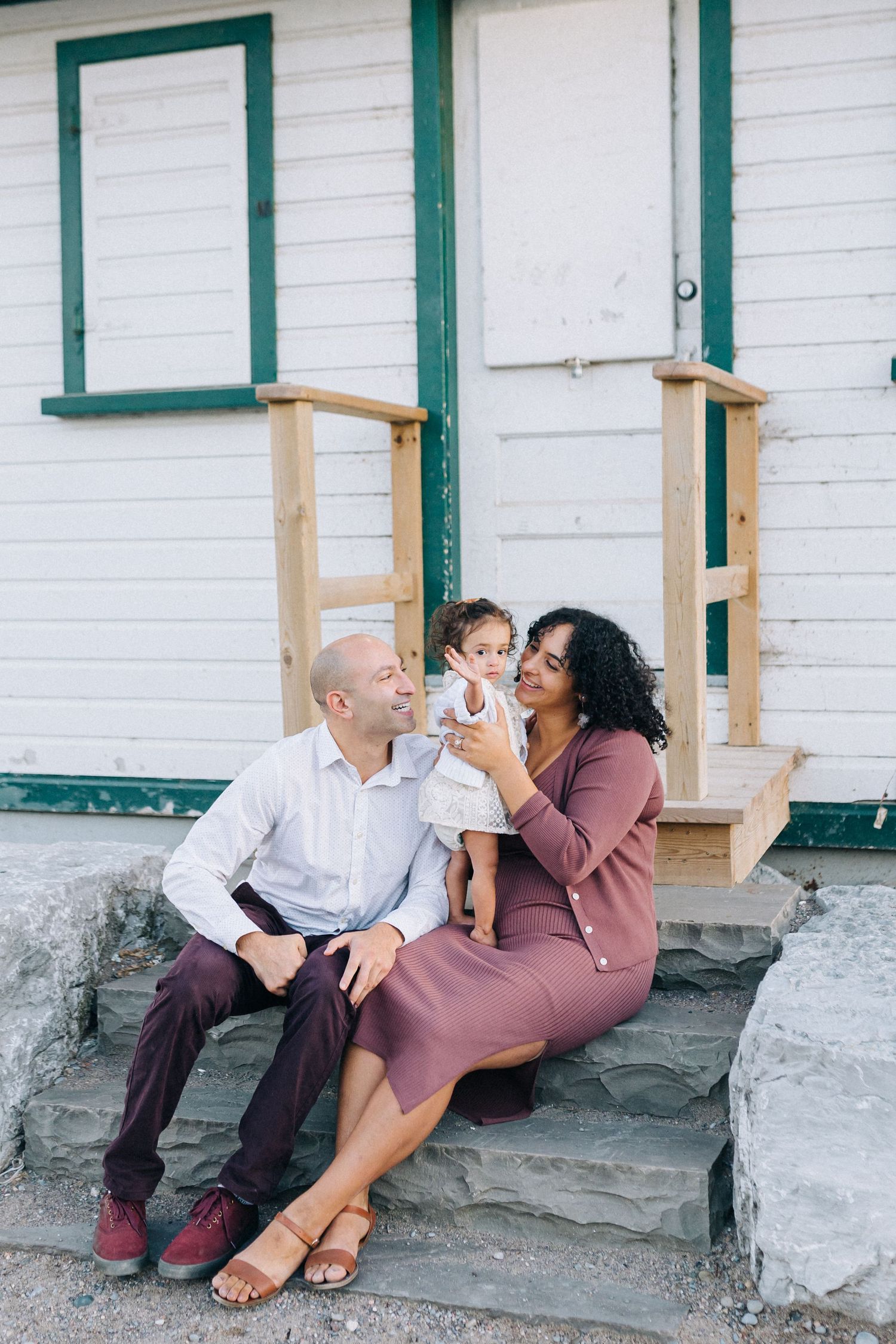 A family sharing a happy moment together on the steps of a white building with green trim.