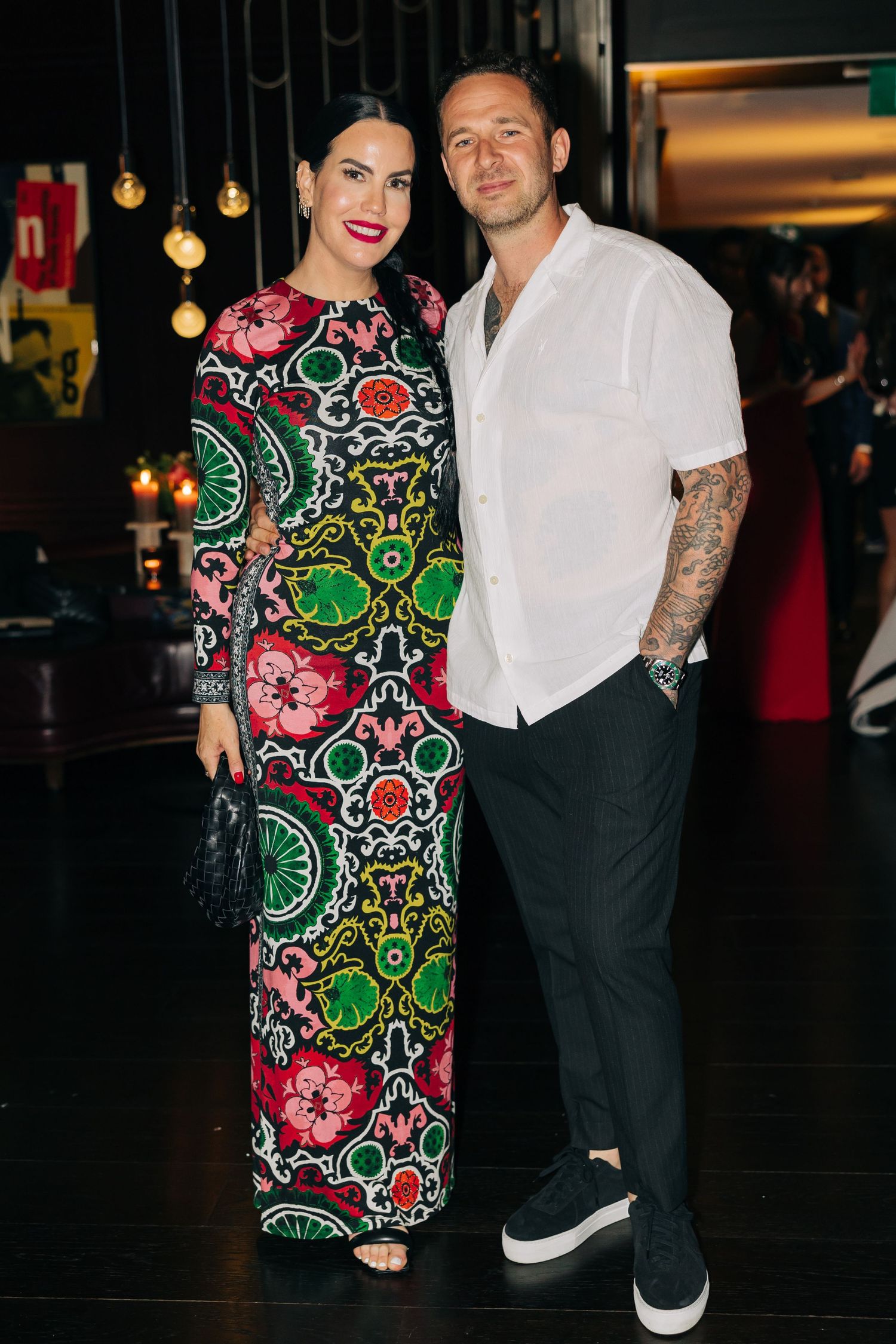 Couple poses together at night event, woman wearing colorful patterned long dress.