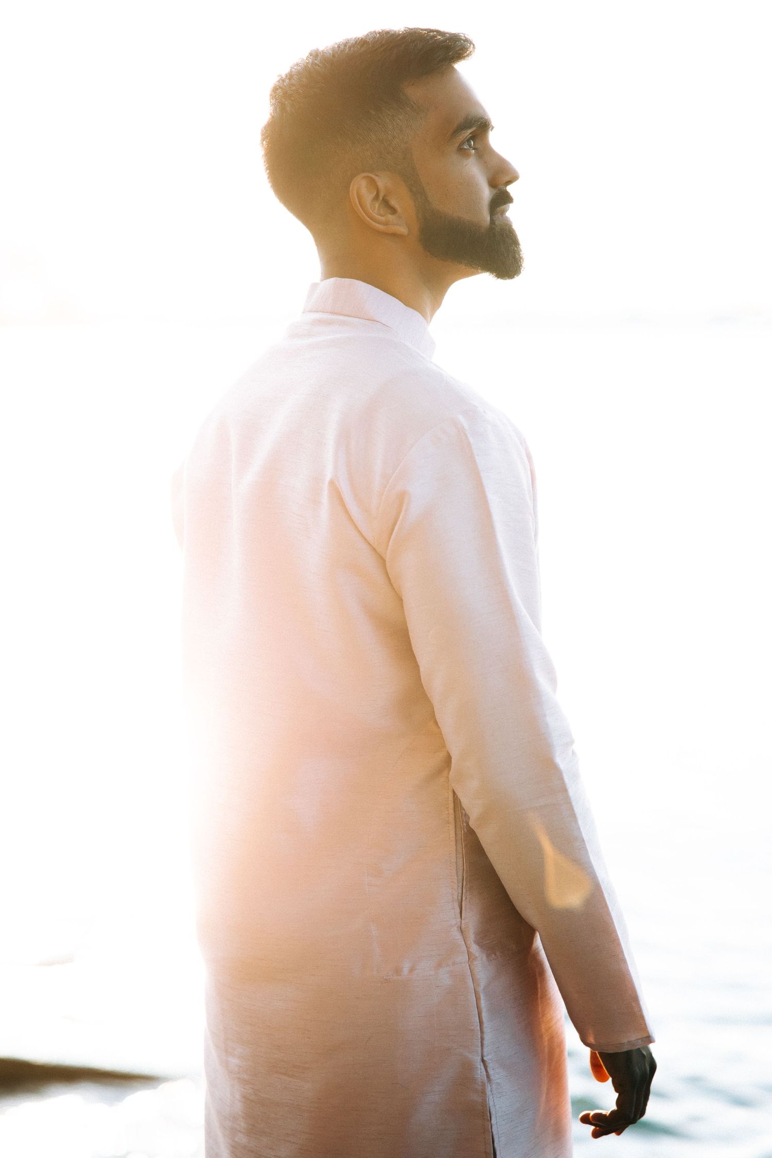 A bearded man in a white shirt stands in profile against a bright backlit sunset.