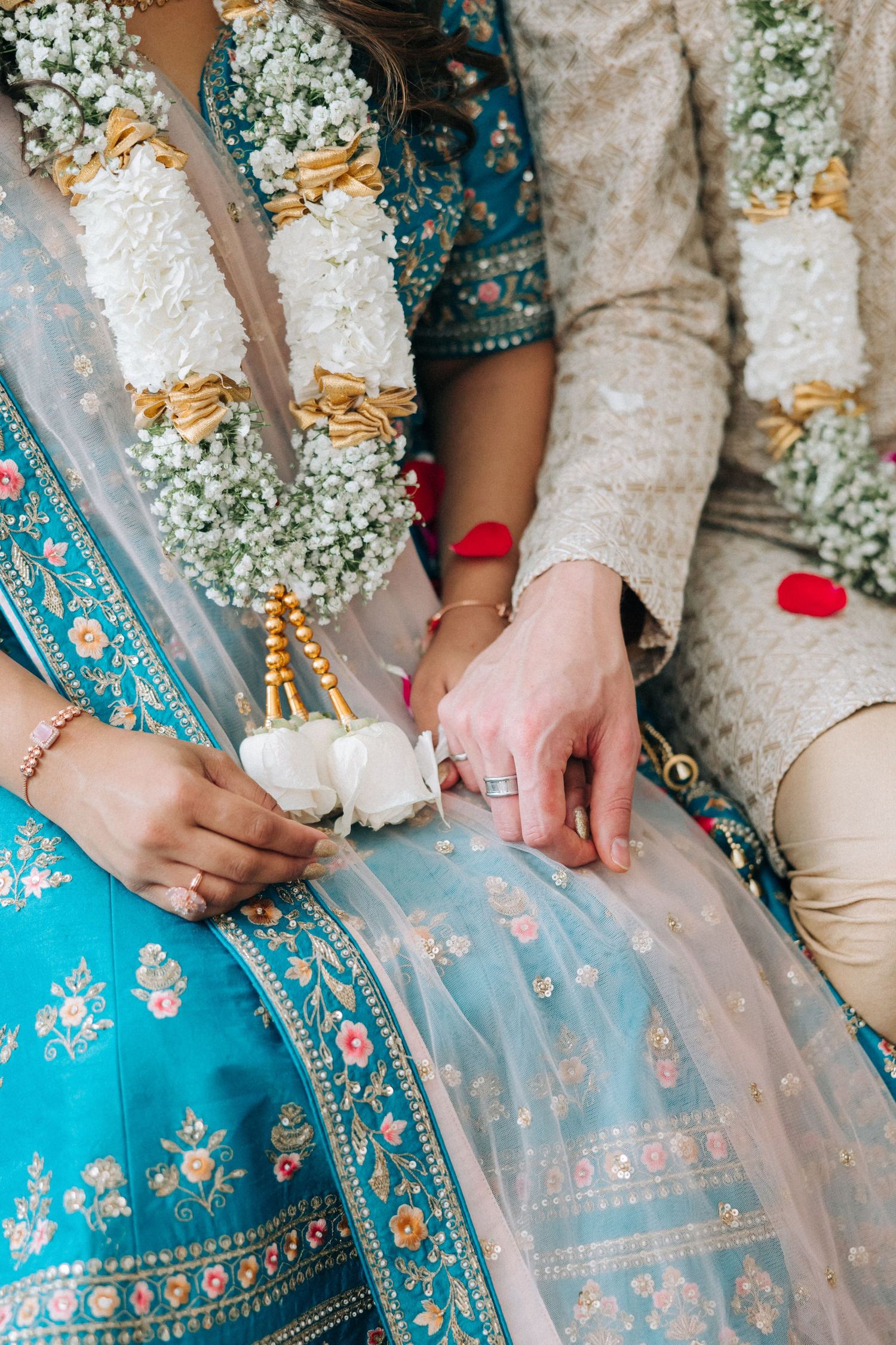 Close-up detail of traditional Indian wedding attire with white and gold flower garlands against turquoise embroidered lehenga.