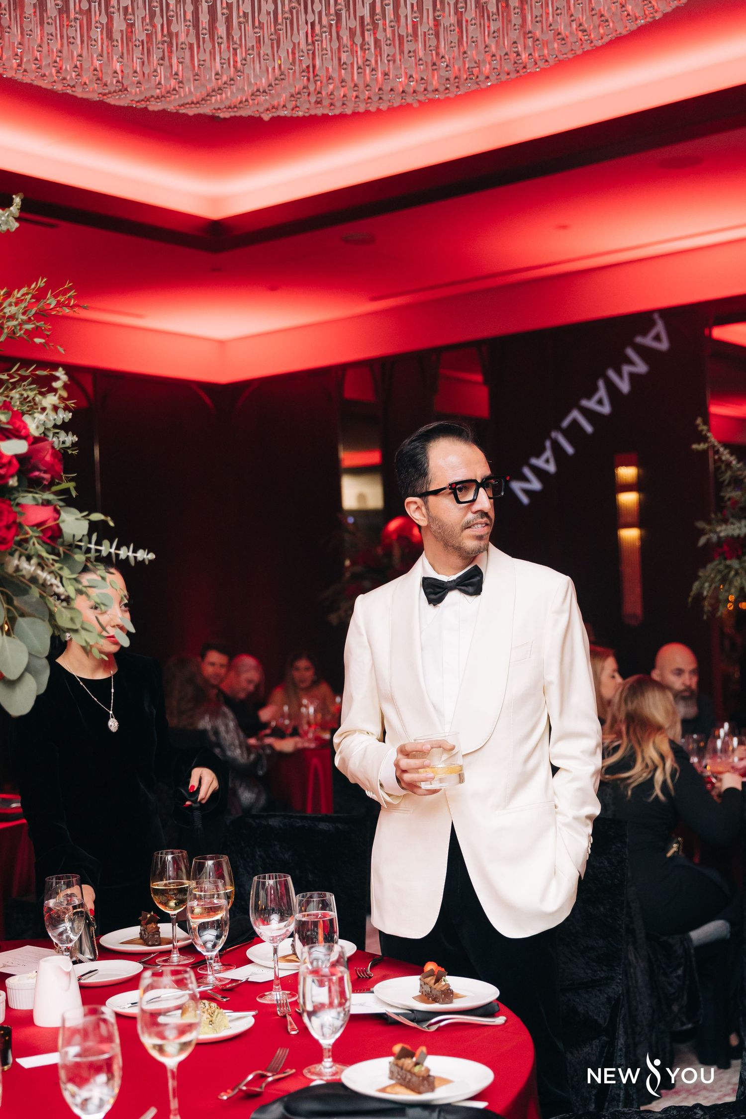 Fine dining event in a restaurant with red ambient lighting and an elegantly dressed guest standing by a formal table setting.