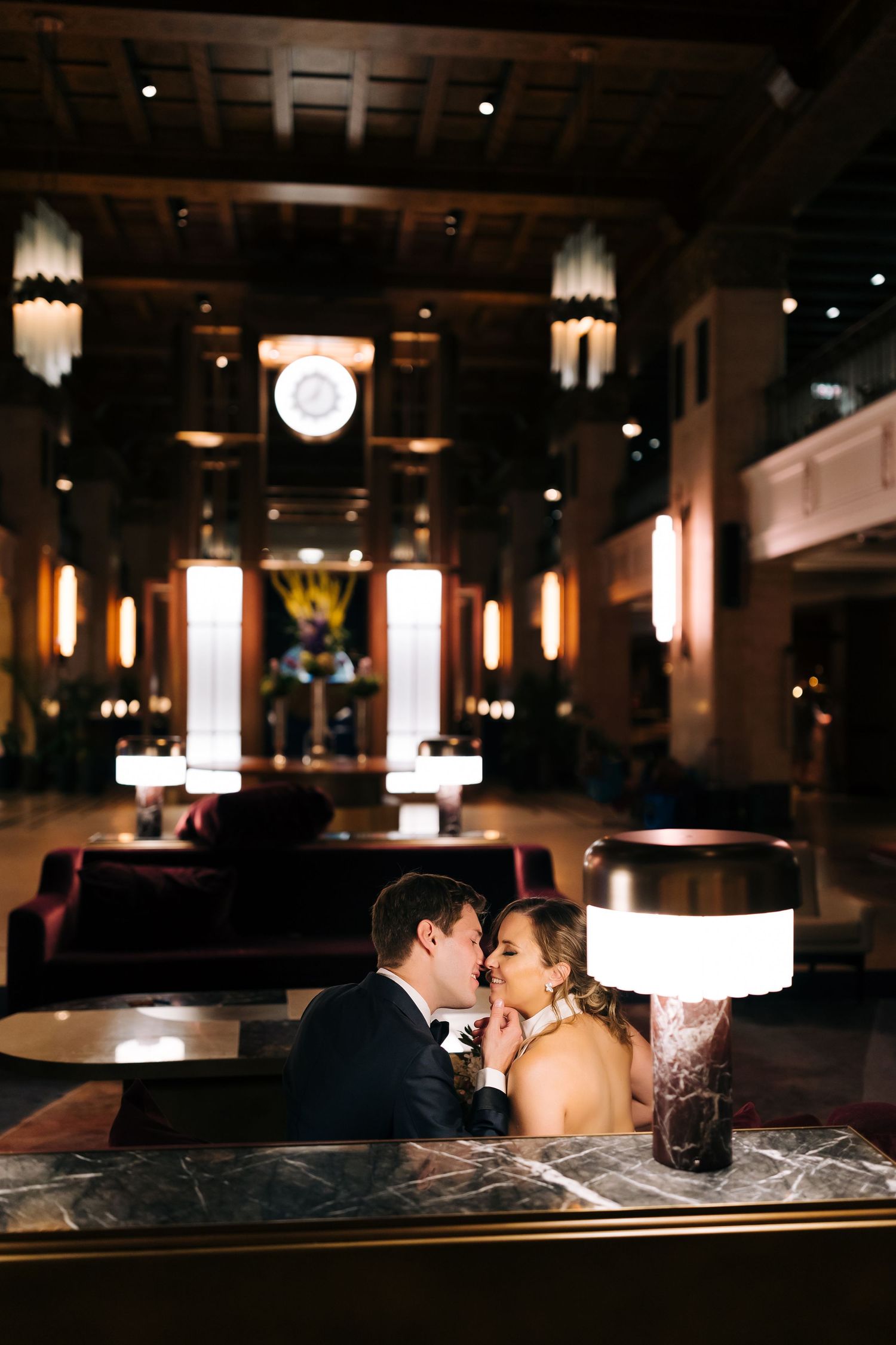 Romantic couple embracing in dimly lit upscale restaurant with art deco lighting and marble tables.