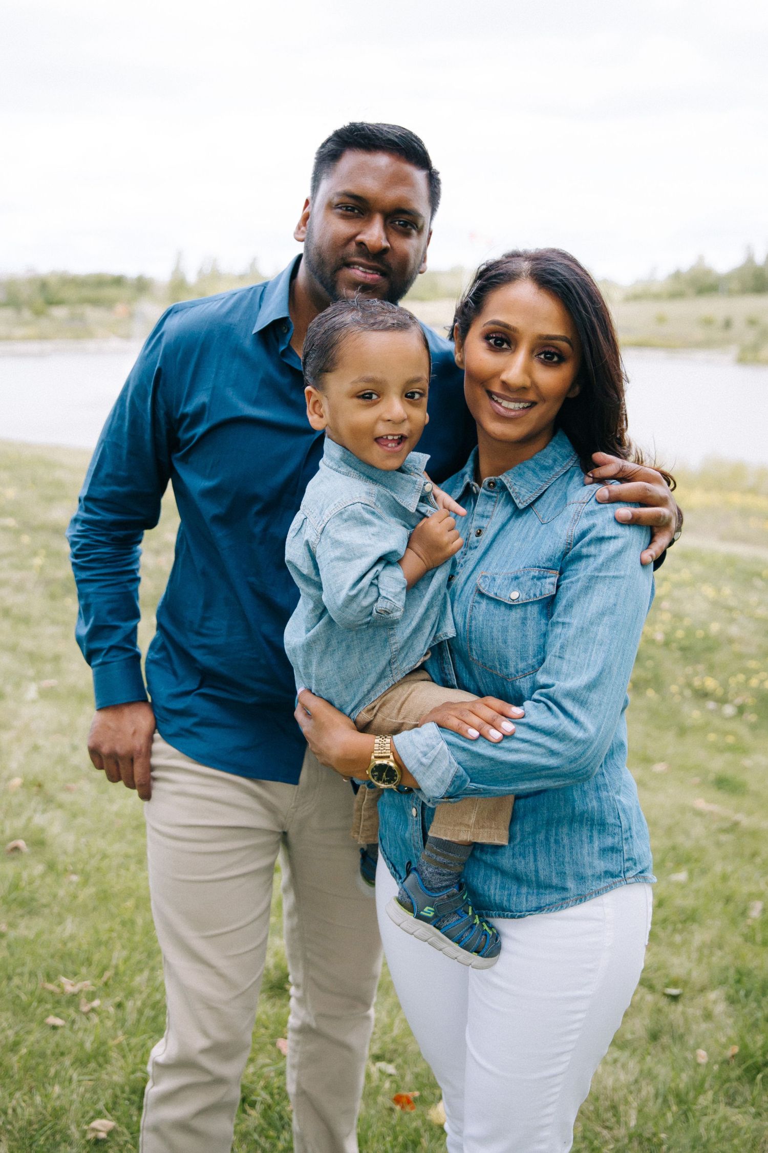 A happy family in matching denim outfits poses together outdoors near a lake.