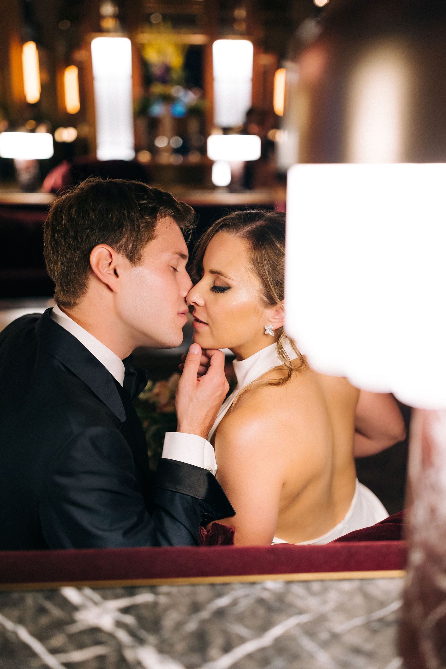 Romantic couple in formal attire sharing an intimate moment in a dimly lit restaurant with glowing pendant lights.