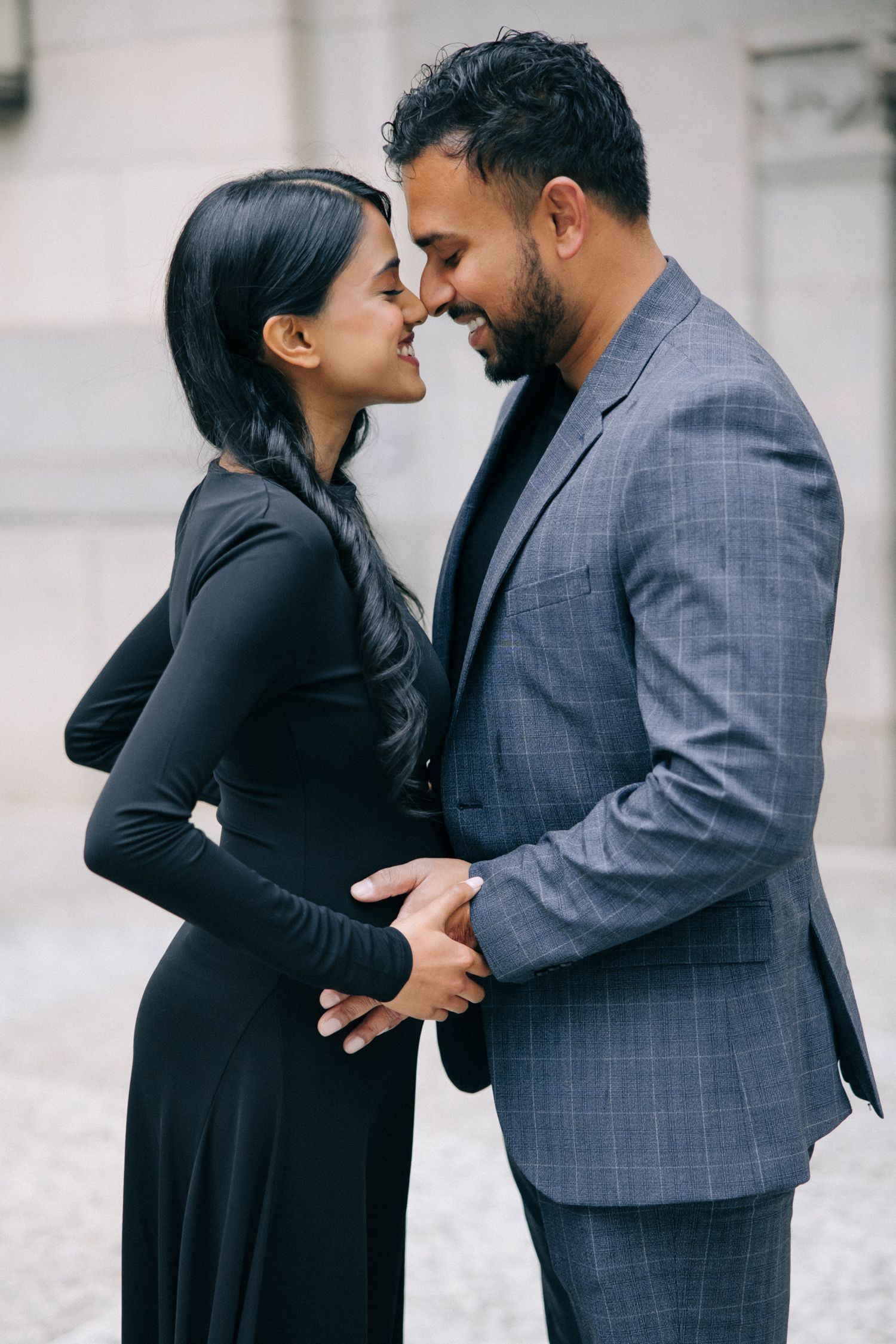 Couple in formal attire share an intimate moment outdoors, with one wearing a dark dress and the other in a gray suit.