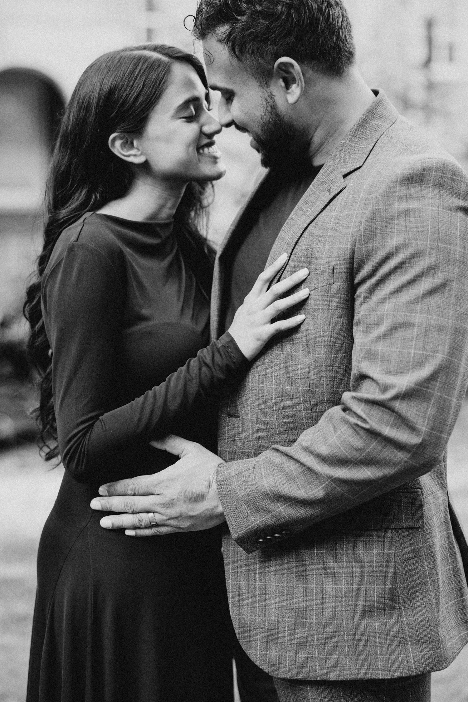 A romantic black and white portrait of a couple in an intimate embrace, with her in a dark dress and him in a blazer.