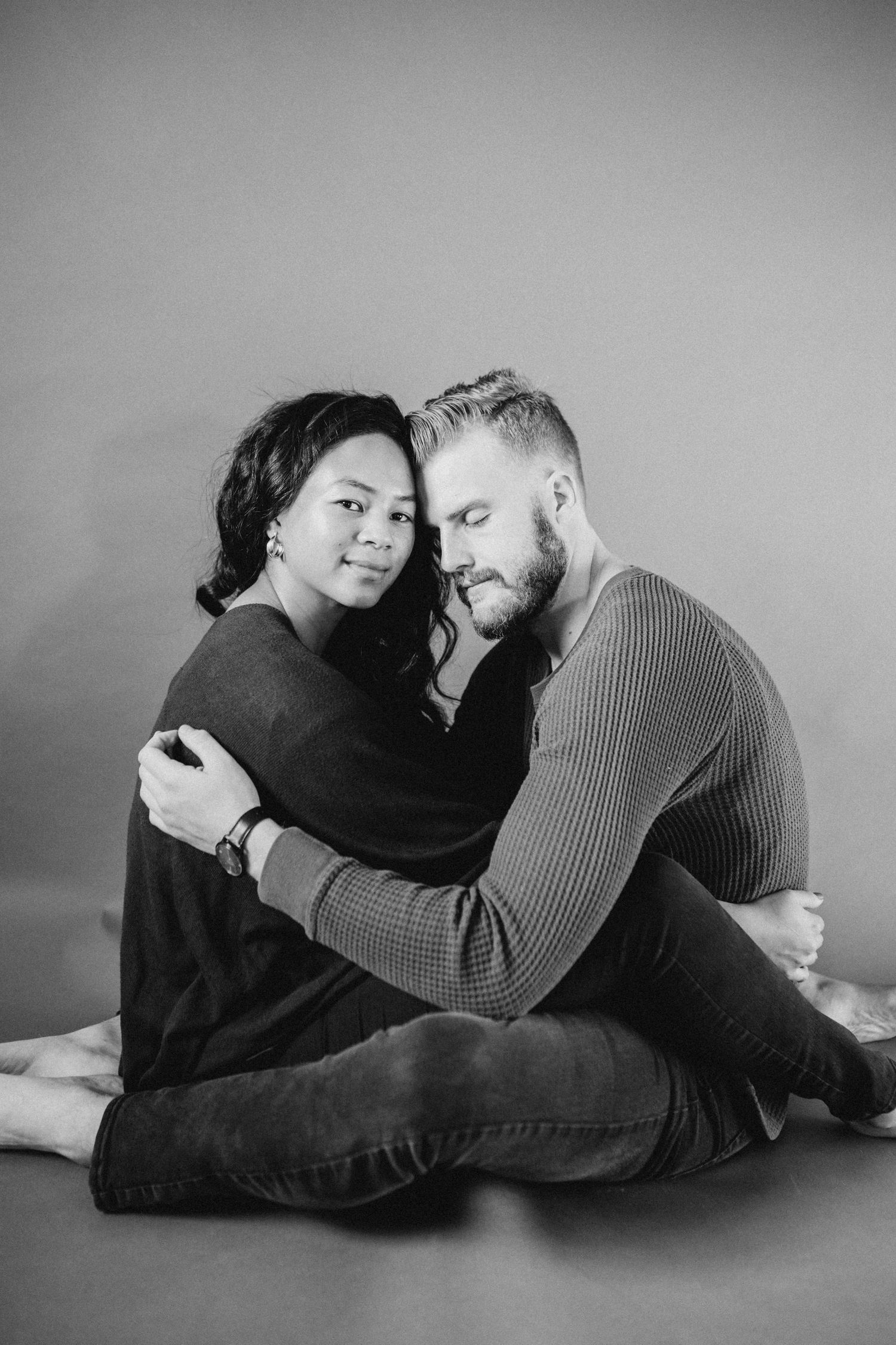 Intimate black and white portrait of couple embracing while sitting on floor.