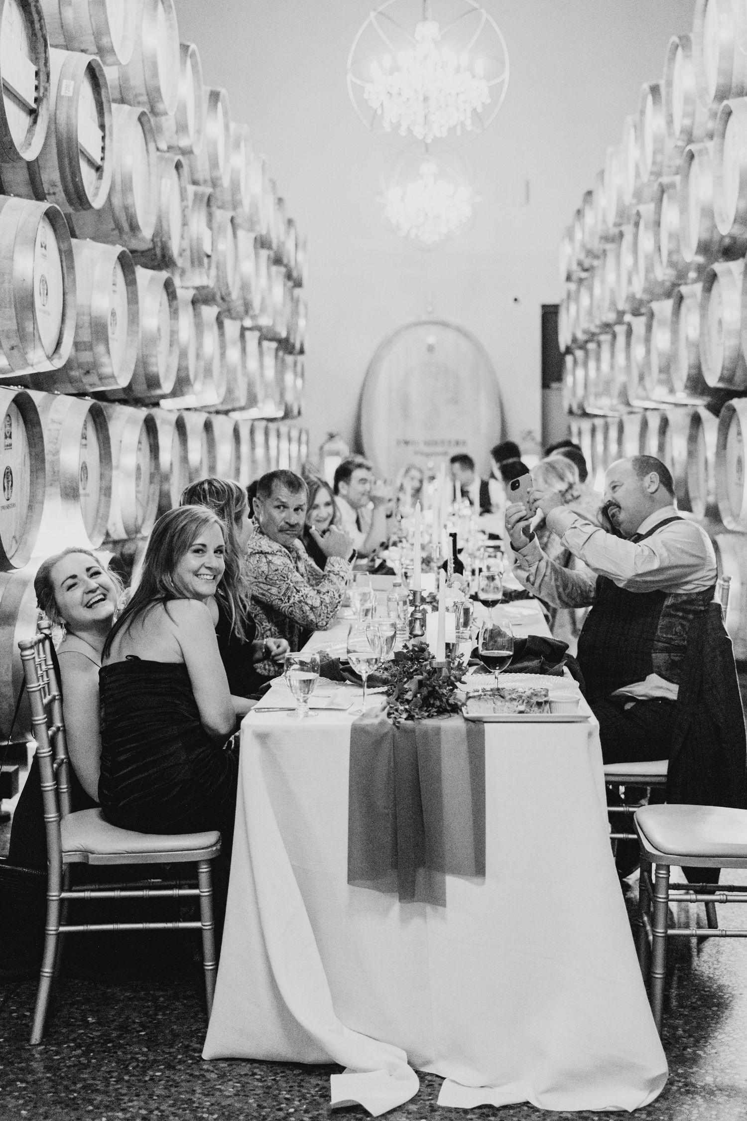 Wedding reception dinner in wine barrel room with elegant table settings and chandelier lighting.