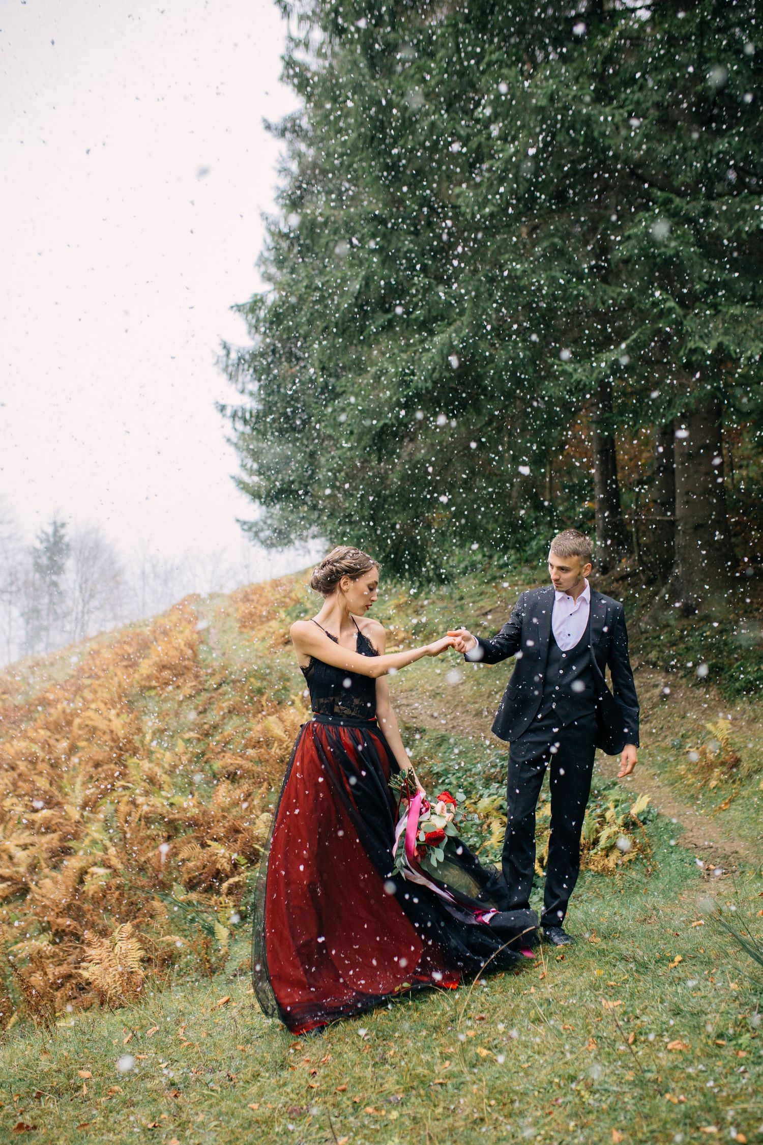 A couple dances in the snow on a hillside, with the woman wearing a dramatic red dress.