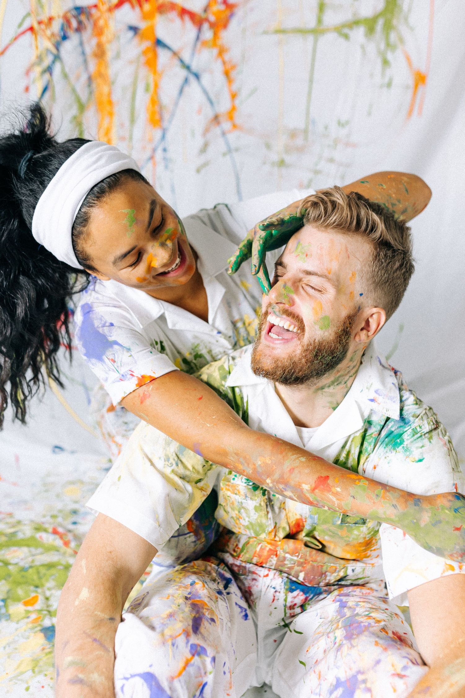 Joyful couple covered in paint laughing and playing during messy paint photoshoot.