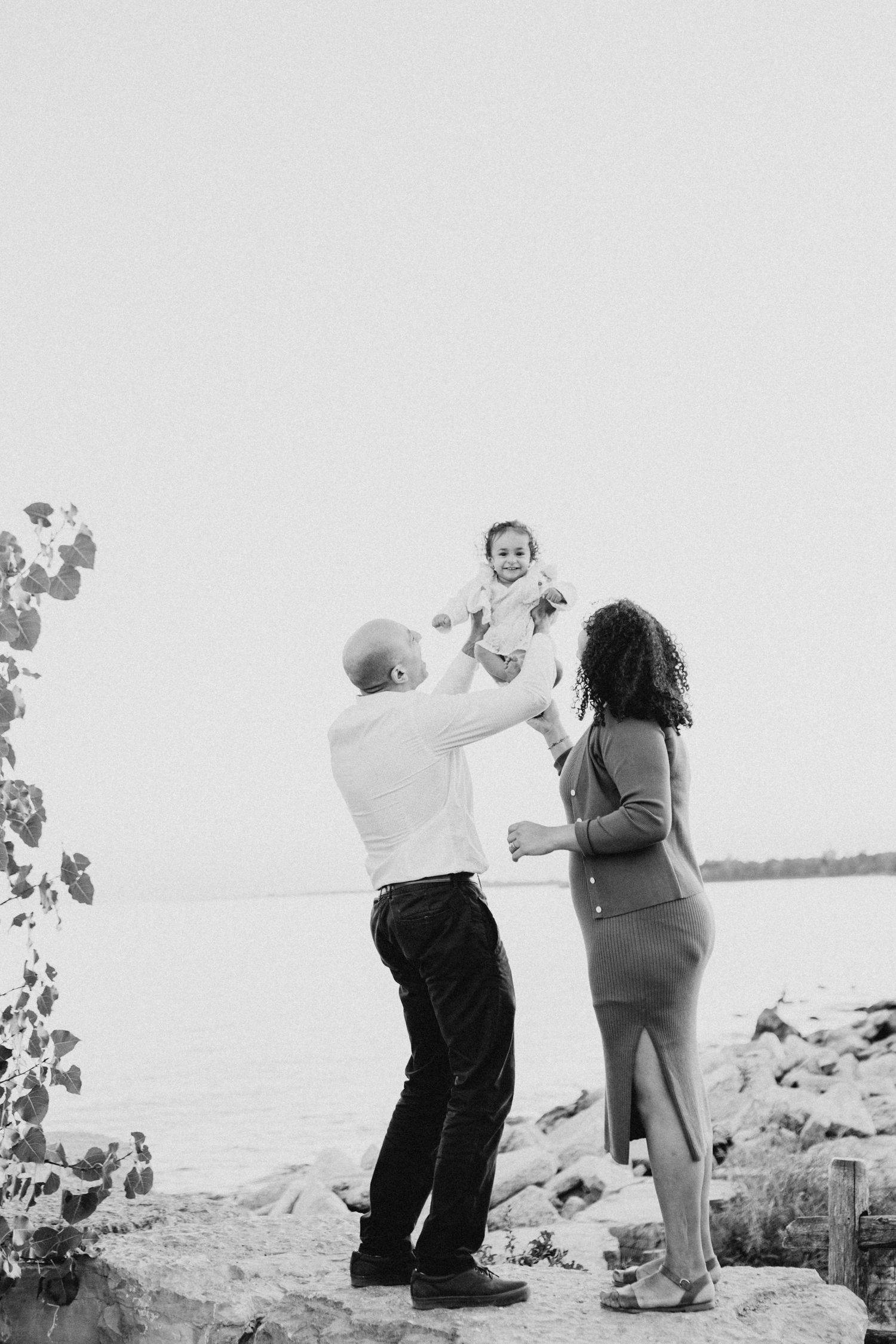 A family shares a playful moment by the waterfront in black and white.