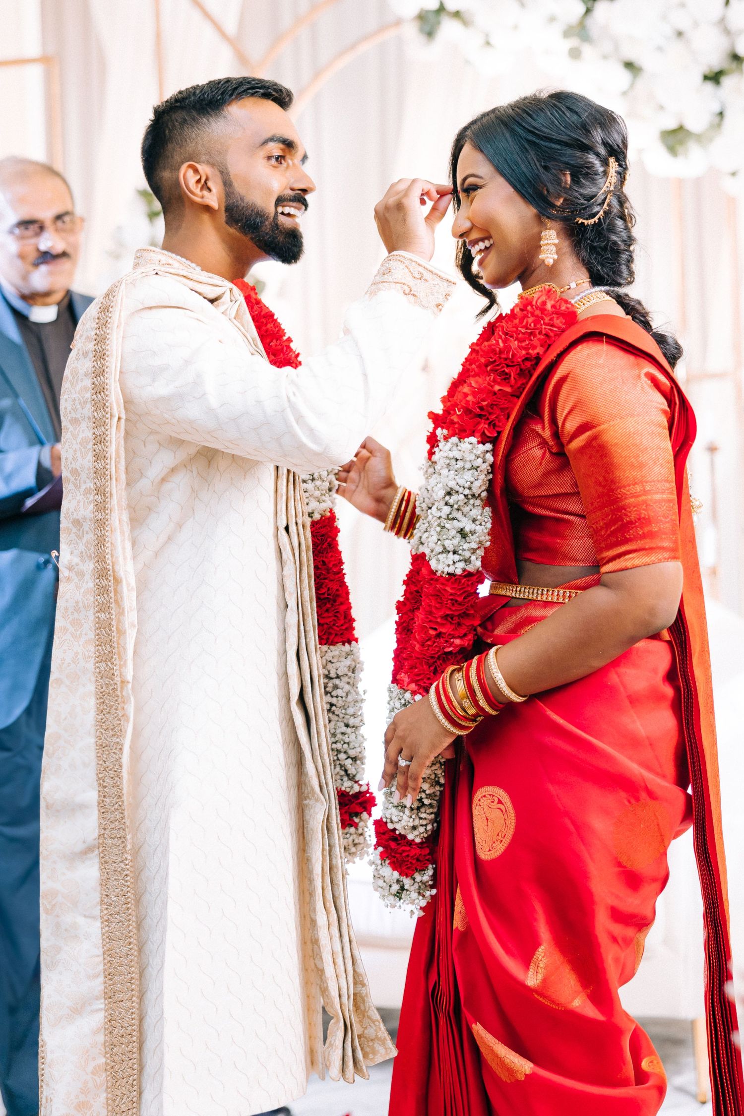 Couple in traditional South Asian wedding attire exchange garlands during a joyful ceremony celebration.