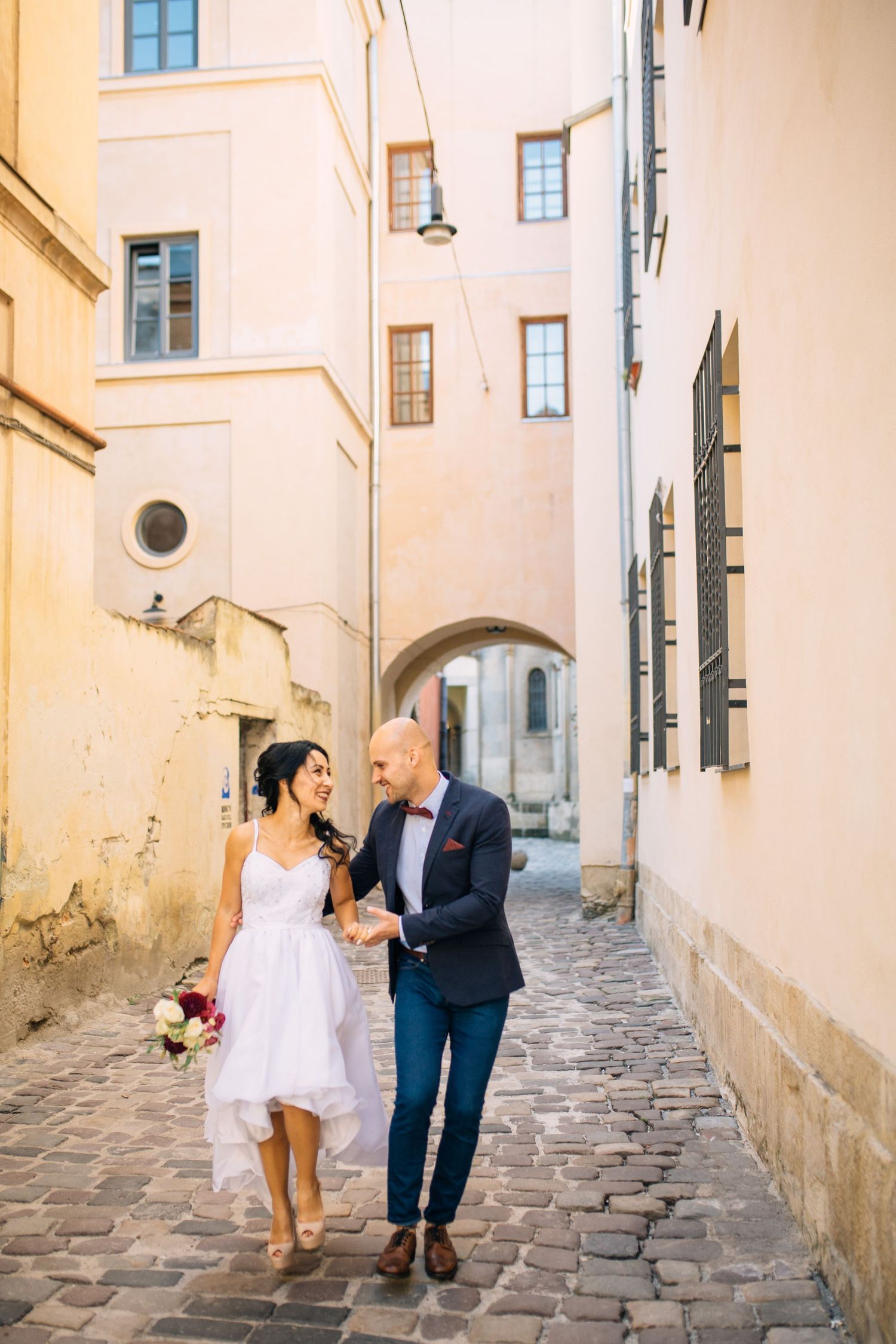 Newlyweds walking hand in hand through a charming European cobblestone alley.