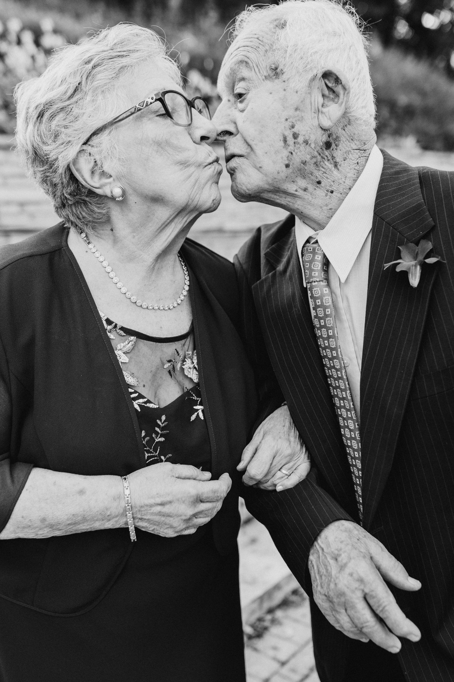 Black and white photo showing an elderly couple sharing a tender kiss while dressed in formal attire at an event.