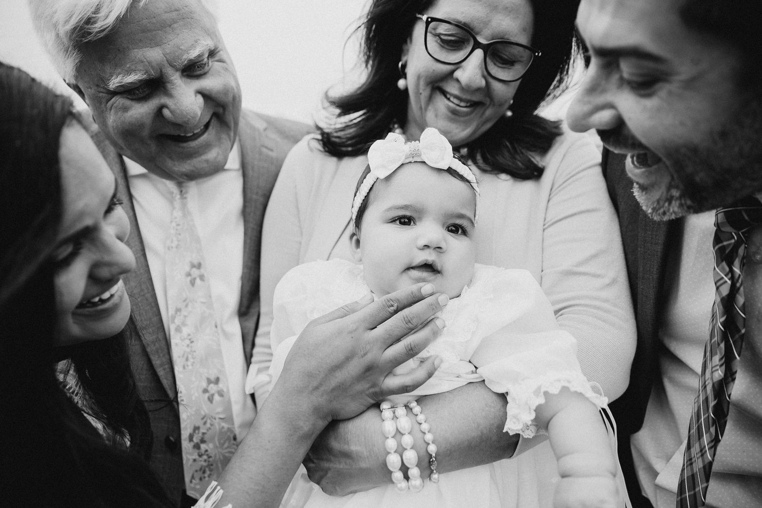 Group of adults joyfully gathered around smiling baby in black and white photo.