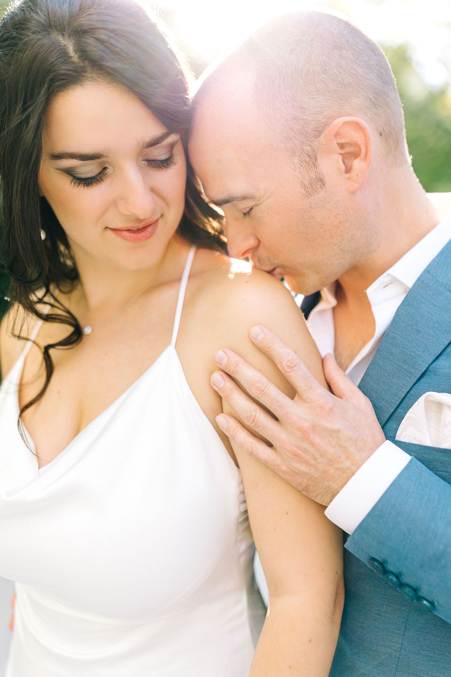 Romantic wedding couple shares an intimate moment outdoors in soft sunlight.