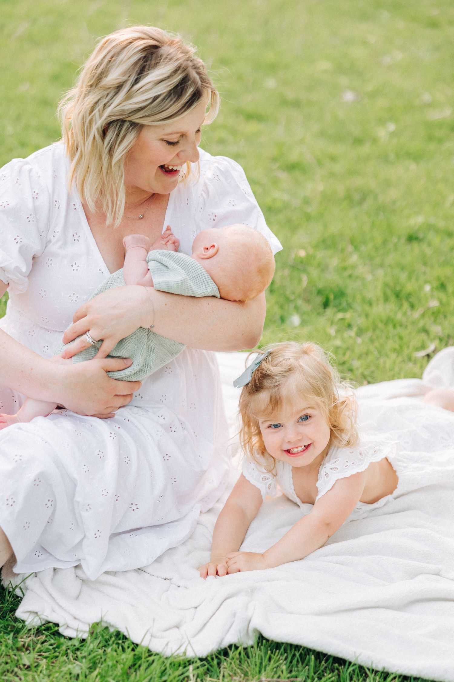 A peaceful outdoor family moment on a white blanket in the grass.