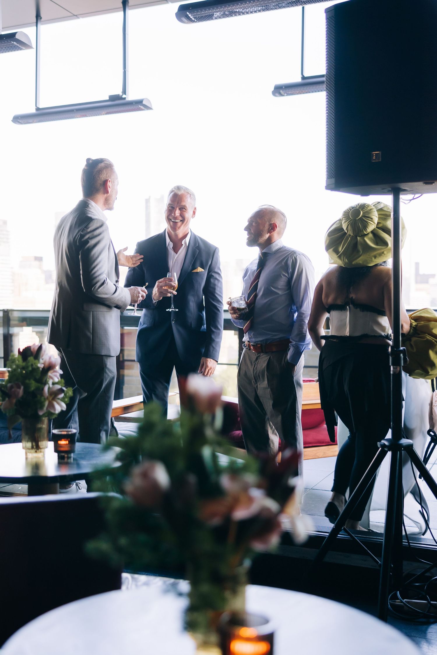 A group of people chatting and holding drinks at an upscale event with floral decorations.