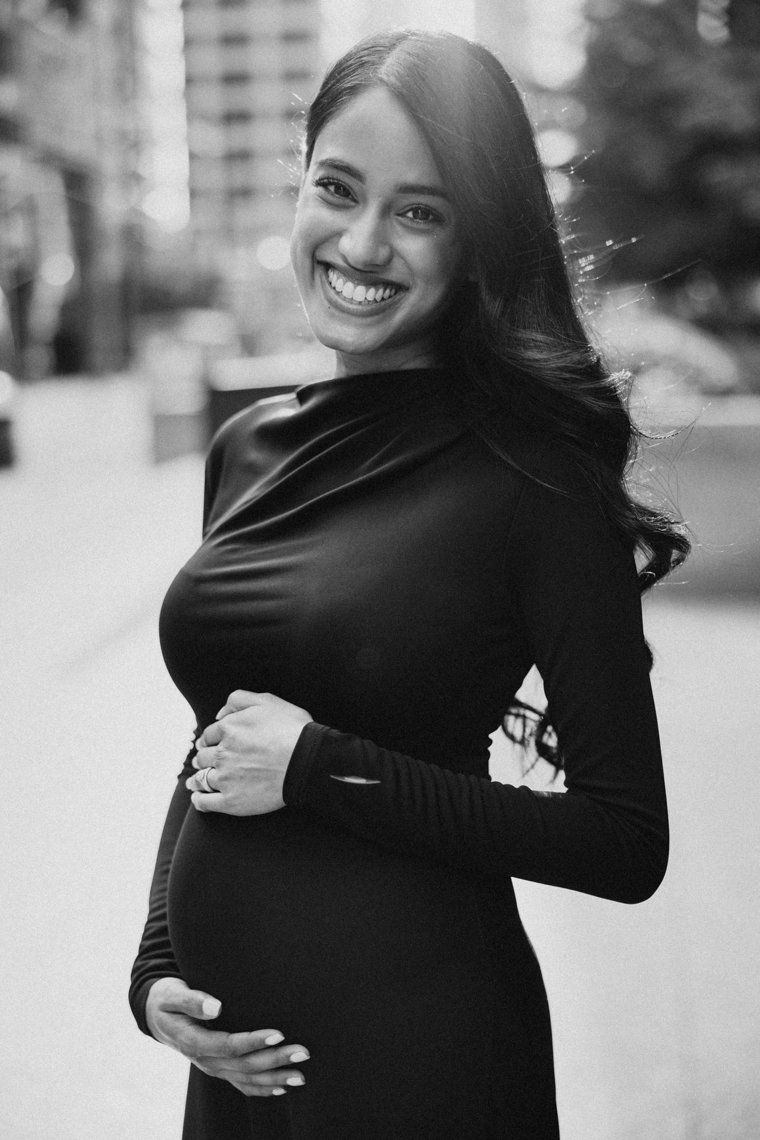Black and white maternity portrait showing radiant smile and baby bump in fitted dress.