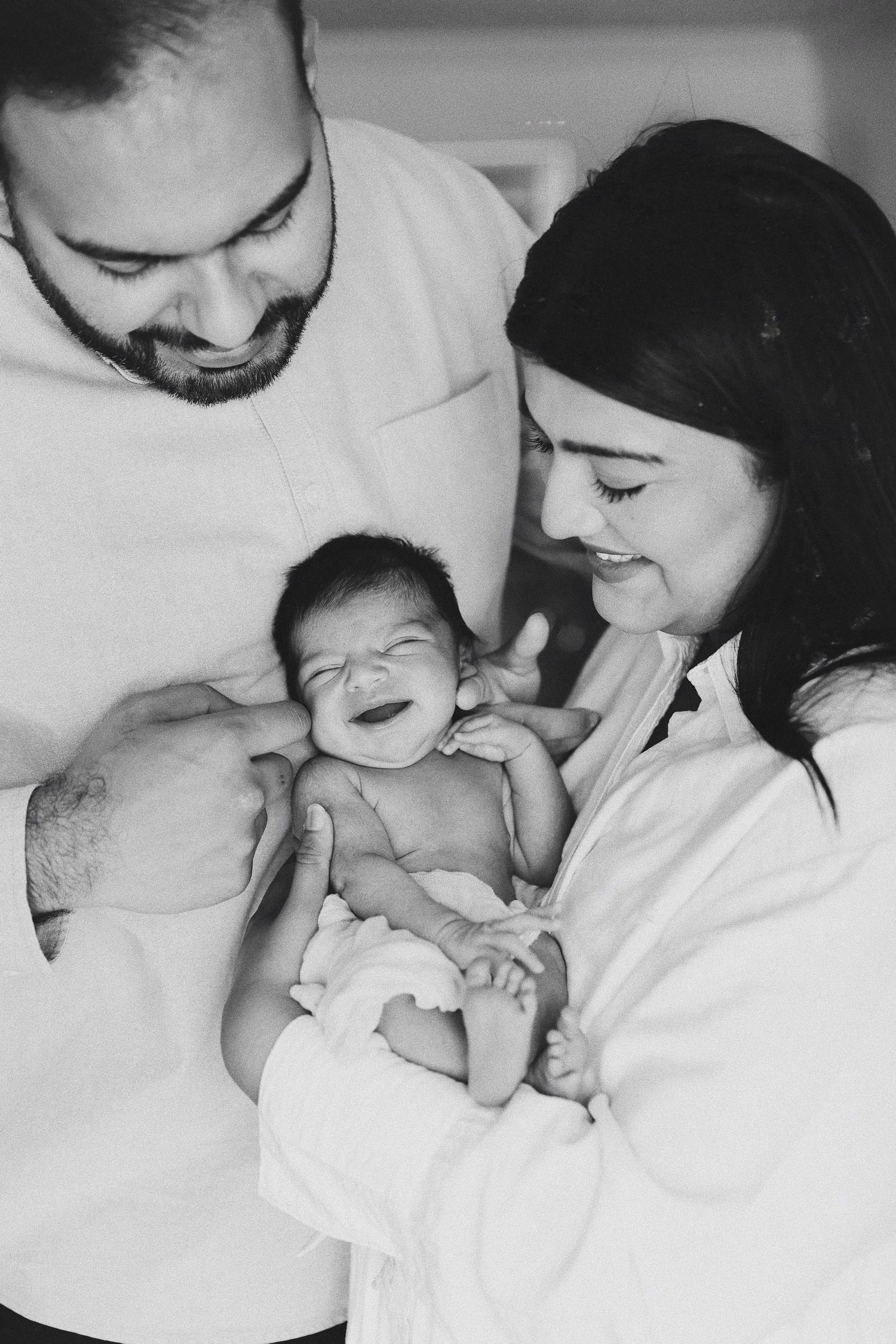 A black and white portrait of new parents with their newborn baby.