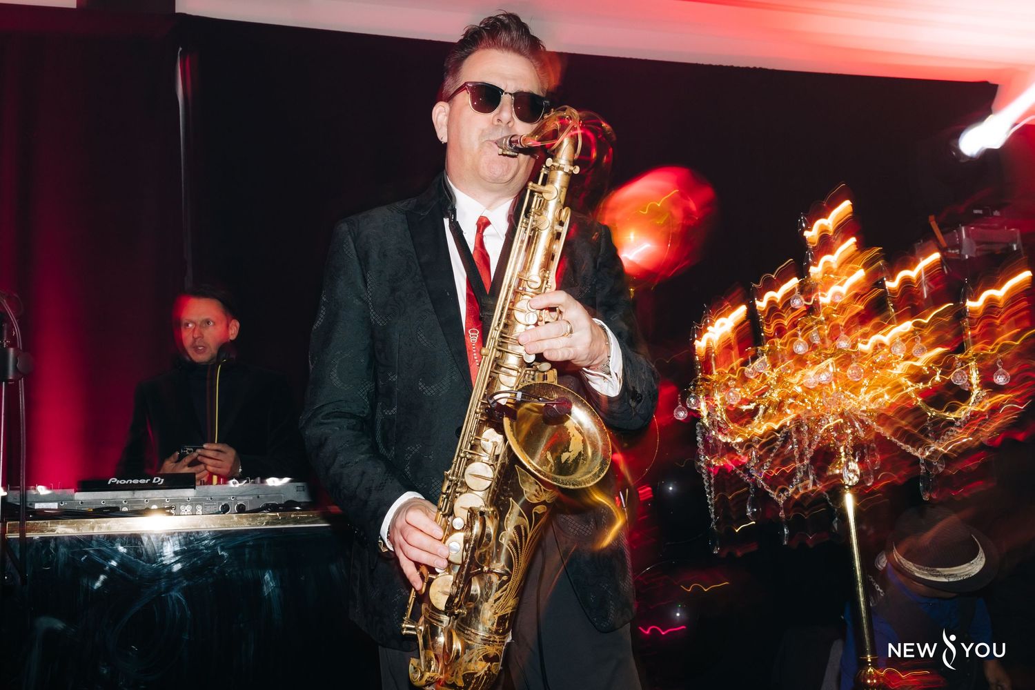 A saxophone performer plays on stage with colorful lighting and sparklers in the background at a nightclub performance.
