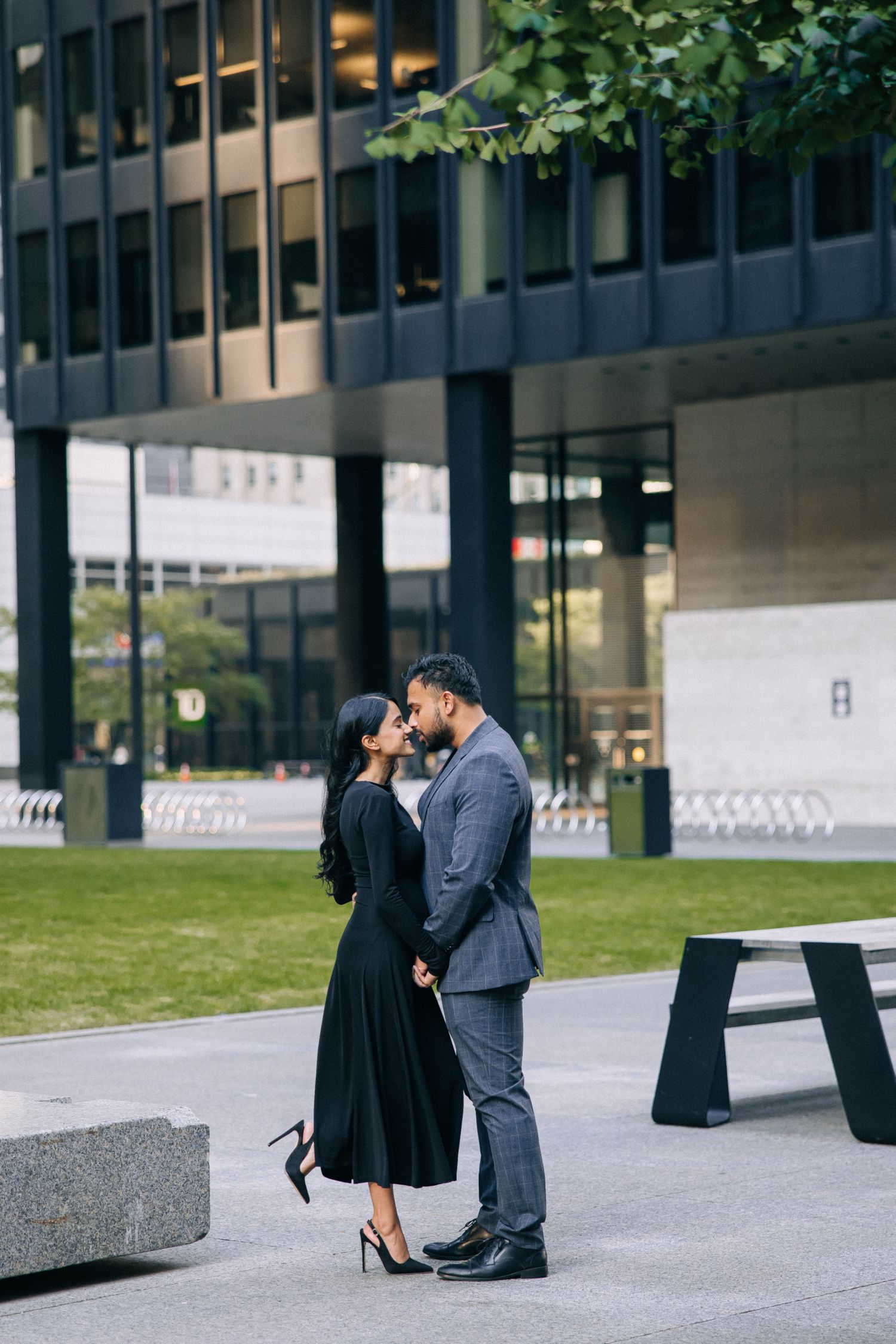 Couple embracing near modern building with glass windows and green lawn.