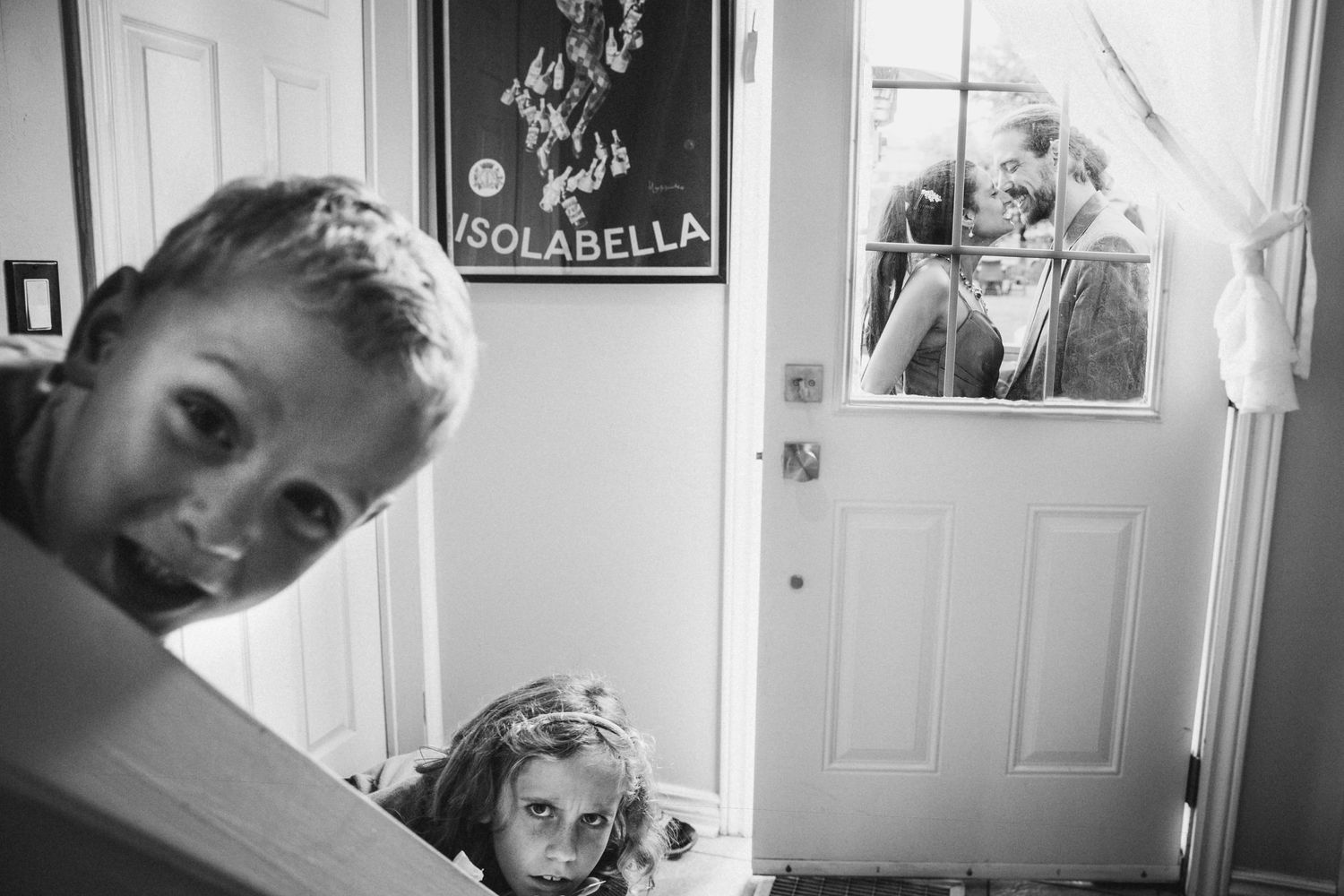 Two children peek playfully through a doorway in a black and white photo.