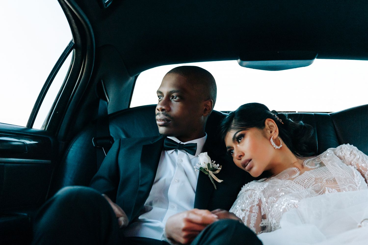 Newlywed couple resting together in the backseat of a car after their wedding ceremony.