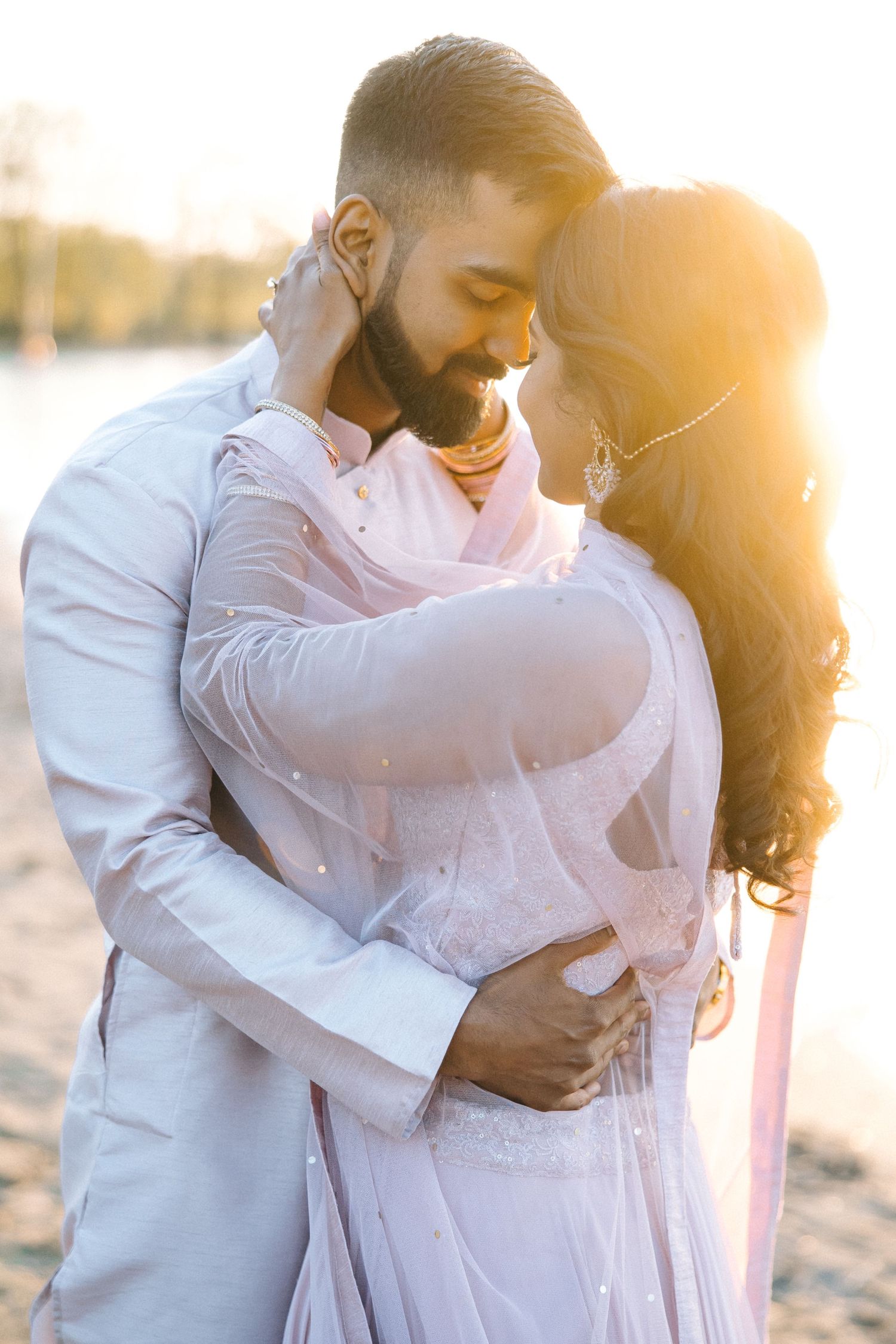 A tender moment between a couple in light pink and white outfits during golden hour.