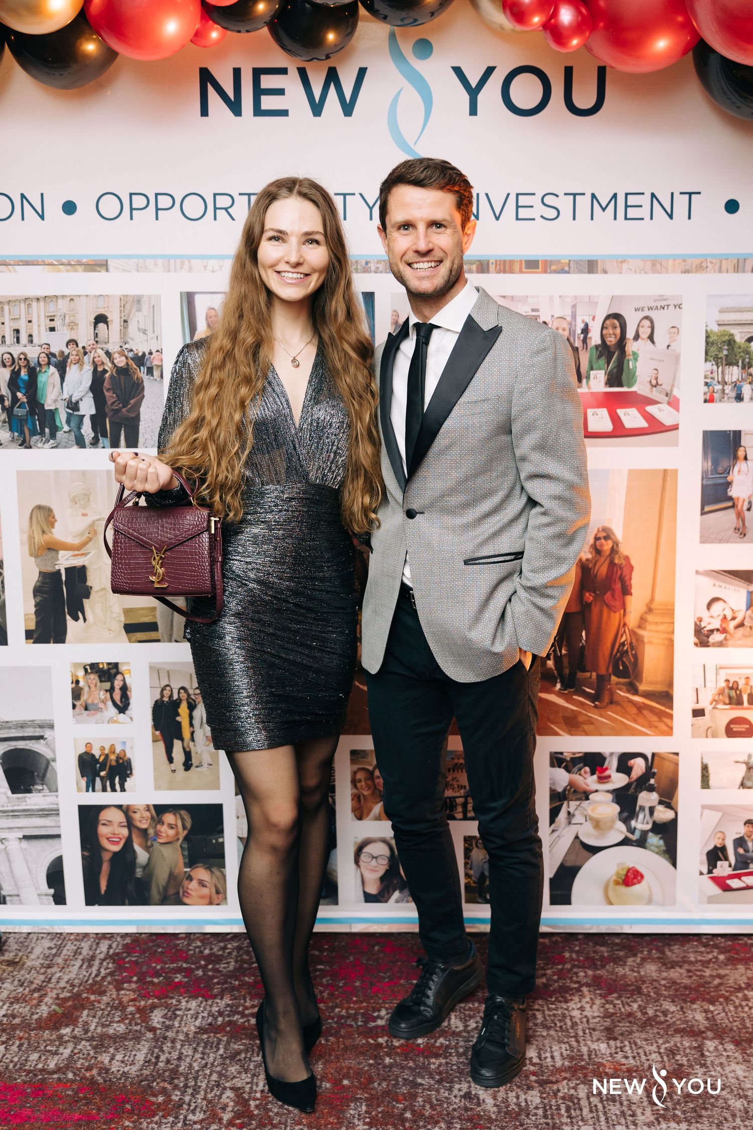 Elegantly dressed couple posing at event backdrop with balloons and 'NEW YOU' text.