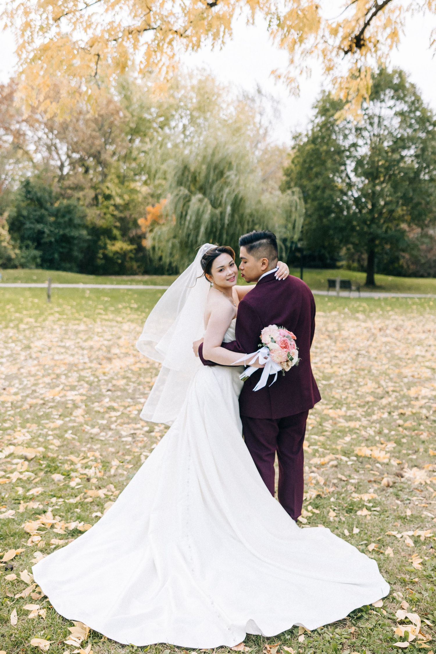 Newlyweds embrace in a fall garden setting with autumn leaves and flowing white wedding dress.
