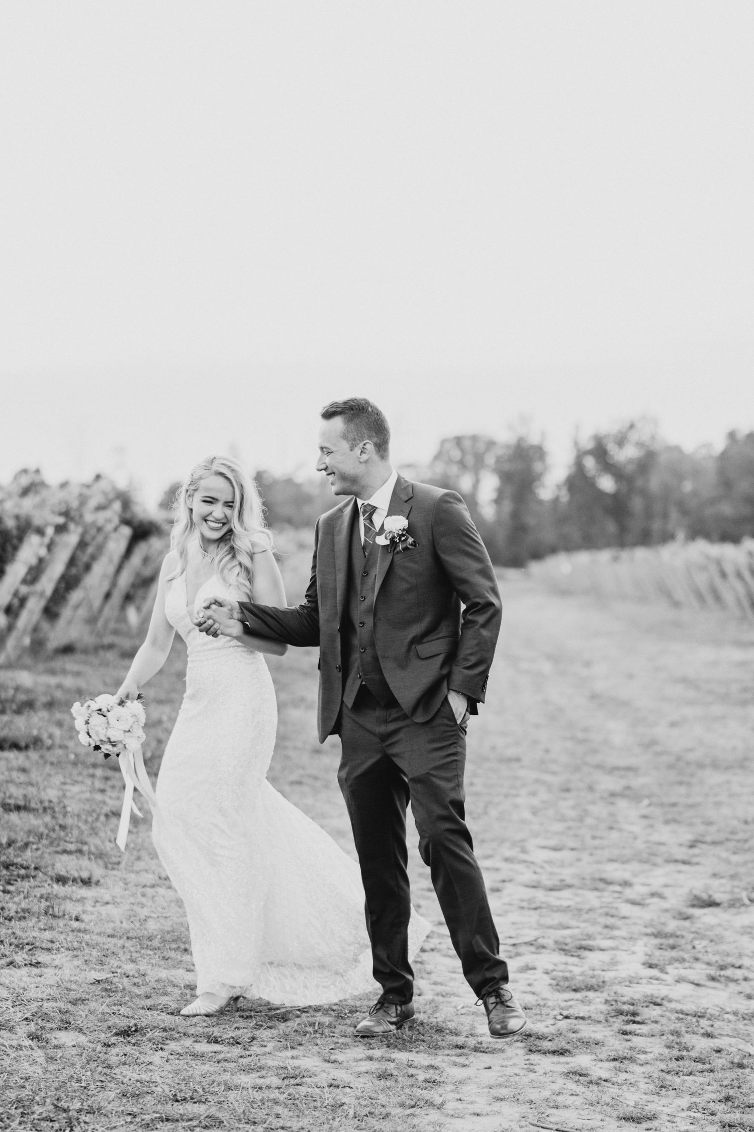 Black and white portrait of couple walking together in vineyard on their wedding day.