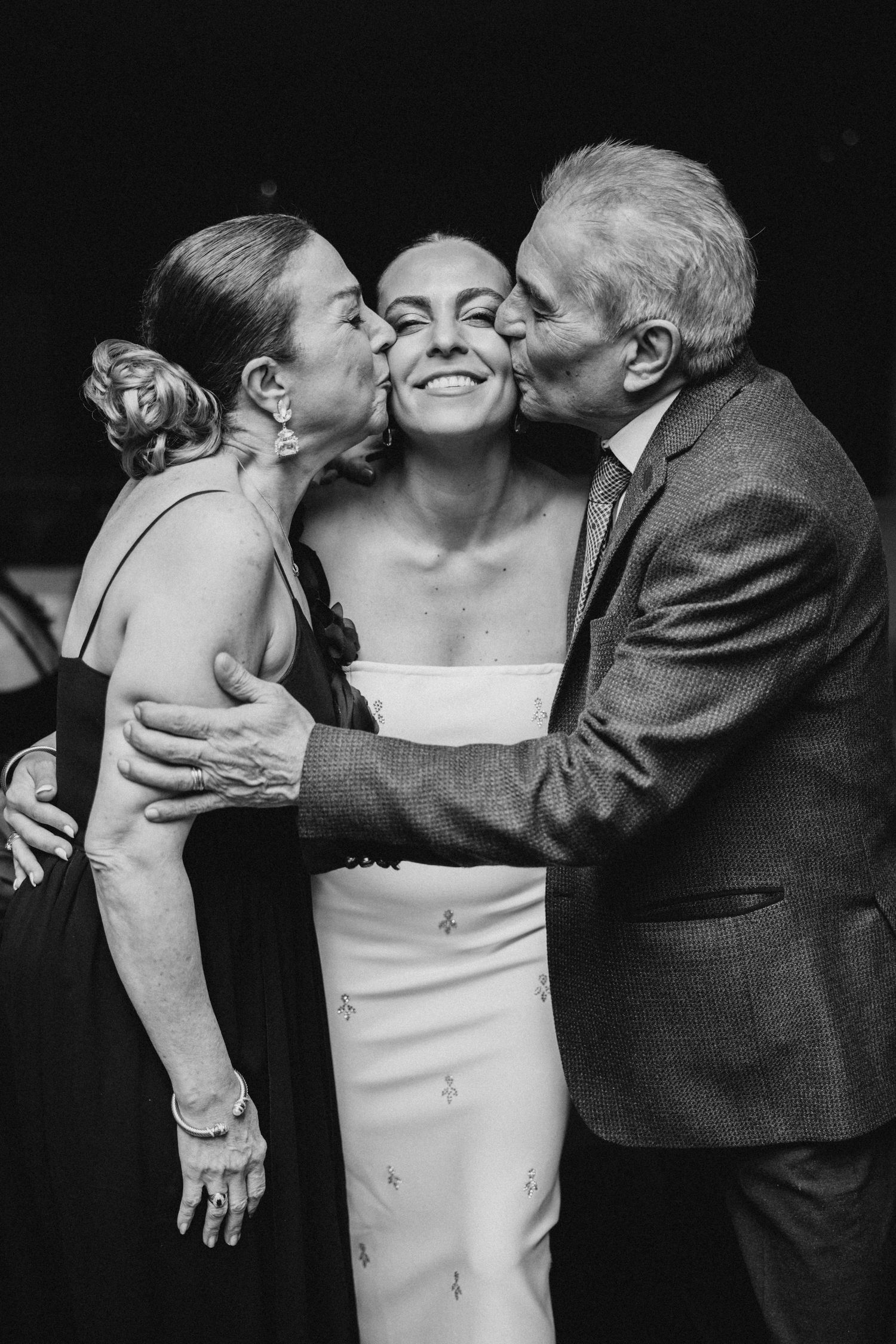 A black and white photo captures a tender moment with a bride being kissed on both cheeks in an emotional embrace.