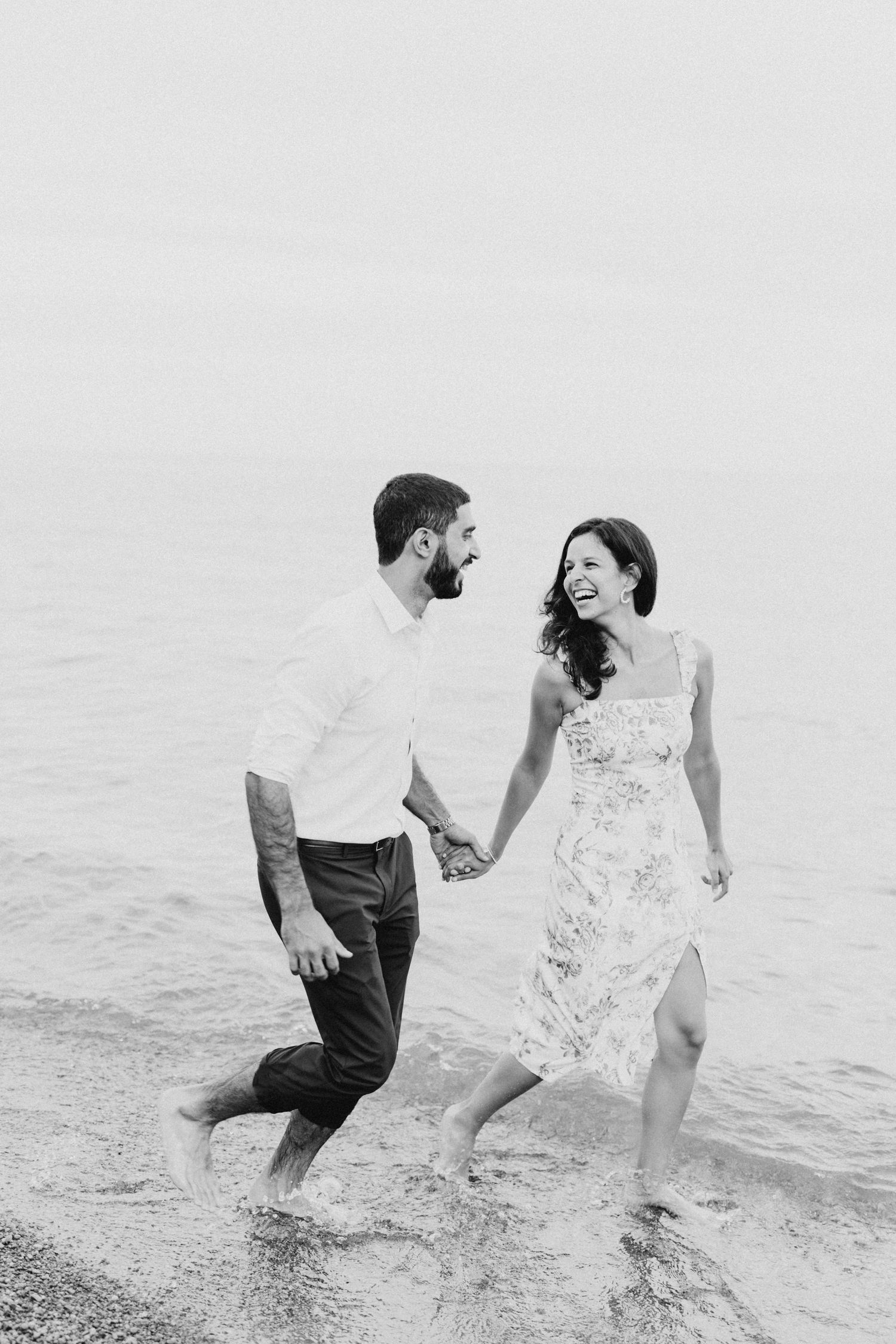A couple laughs while walking through shallow water at the beach.