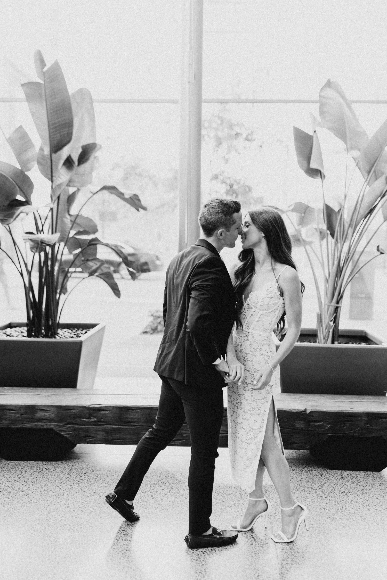 Black and white portrait of couple near indoor plants in modern space.