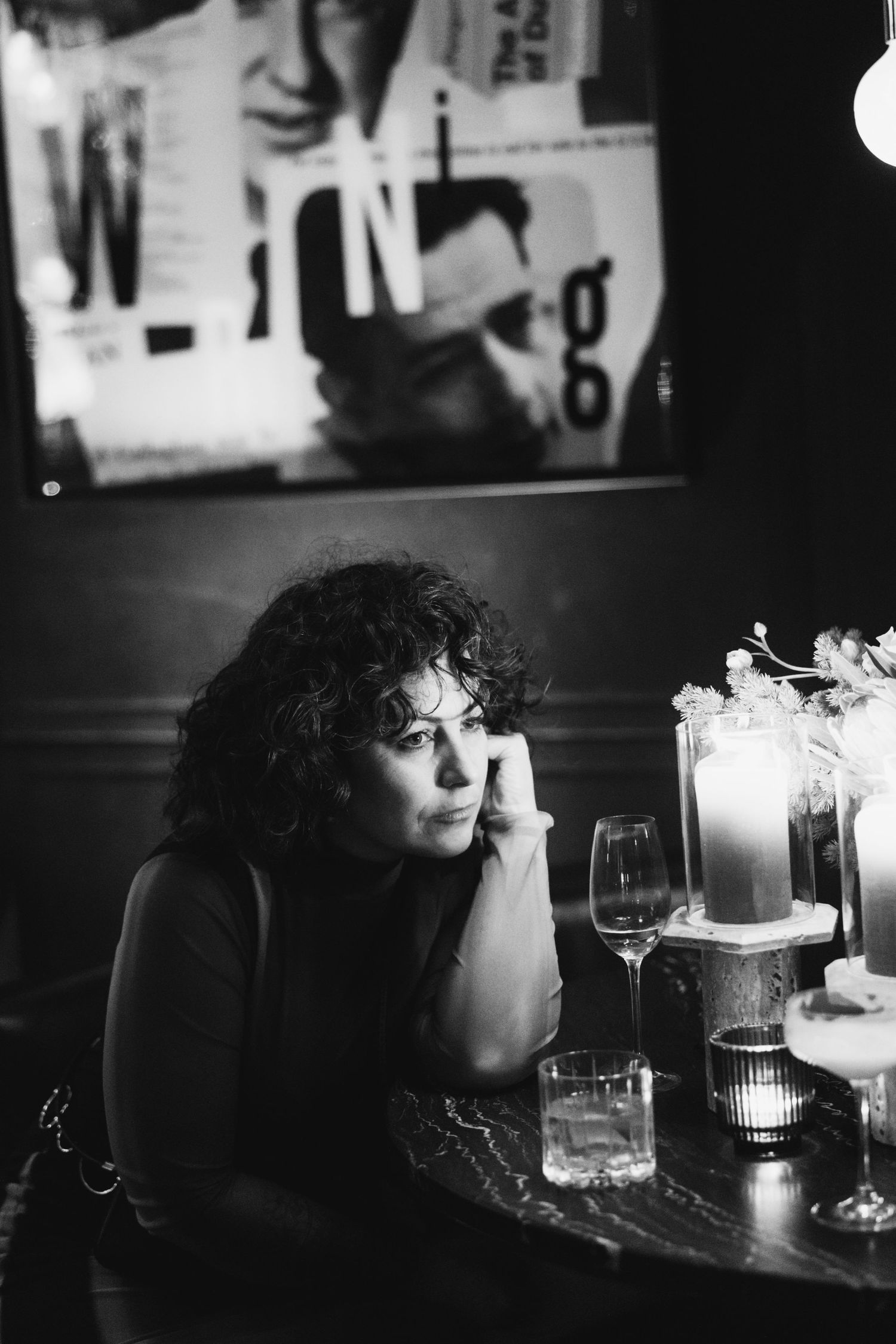Moody black and white portrait of someone deep in thought at a table with candles.